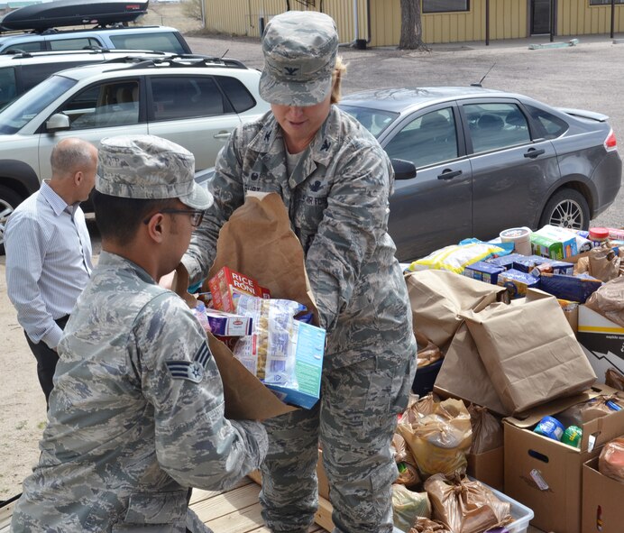 Col. DeAnna Burt, 50th Space Wing commander (right), transfers food to Senior Airman Matthew Sarangay, 50th Contracting Squadron, during a donation drop-off at the Ellicott Helping Hands Food Pantry in Ellicott, Colorado, Tuesday, April 26, 2016. The food was collected by the Schriever Air Force Base Teens/Kids Helping Kids group during a food drive at the Peterson Air Force Base commissary April 23-24. The group raised more than $350 and 2,149 pounds of food to benefit local families. (U.S. Air Force photo/Brian Hagberg)