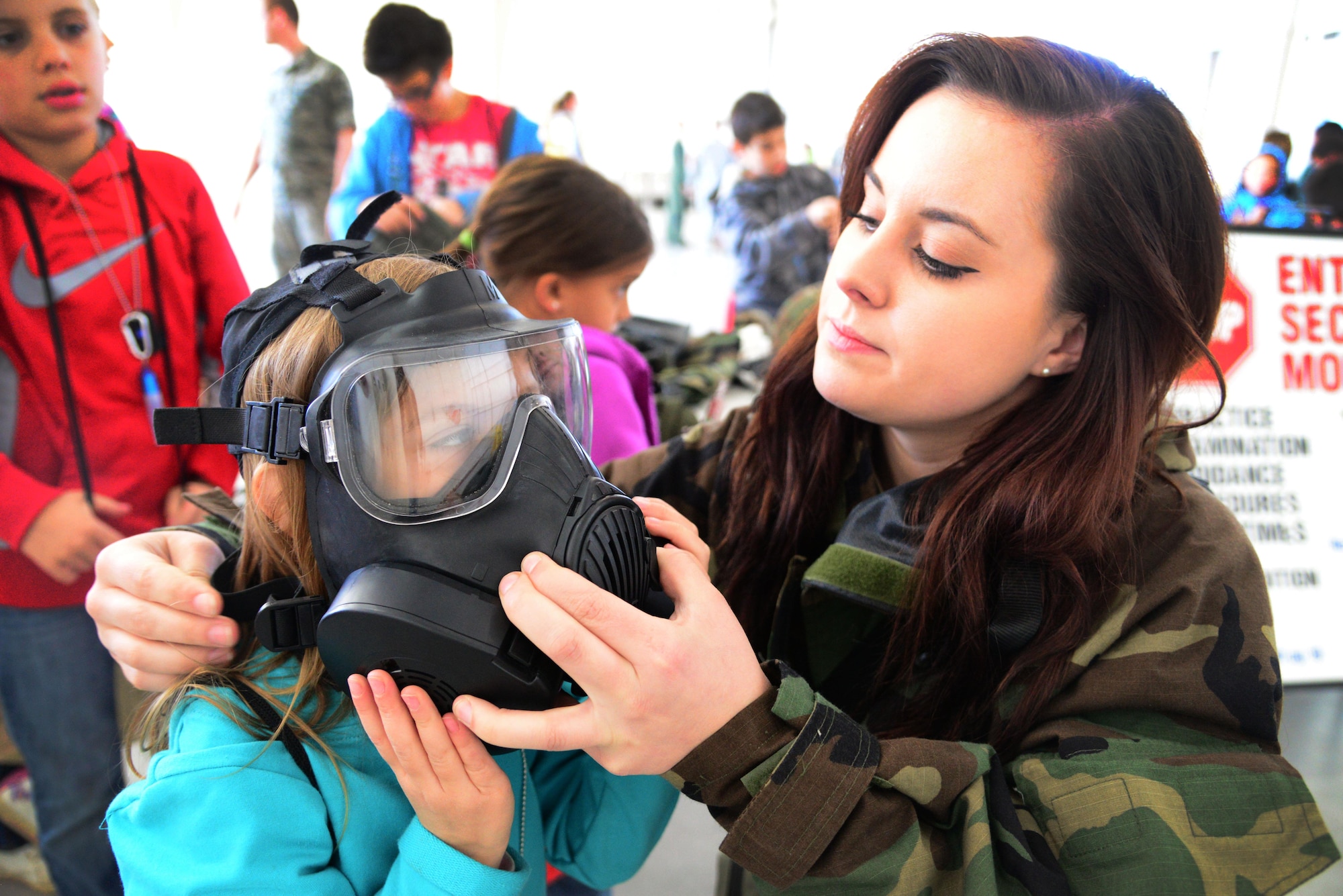 Airman 1st Class Amanda Kopecky, 27th Special Operations Civil Engineer Squadron emergency management, helps a child try on a gas mask during Operation KUDOS (Kids Understanding Deployment Operations) April 30, 2016, at Cannon Air Force Base, N.M. Children interacted with multiple agencies and displays to better understand their roll in the wing’s mission. (U.S. Air Force photo/Staff Sgt. Alexx Pons) 