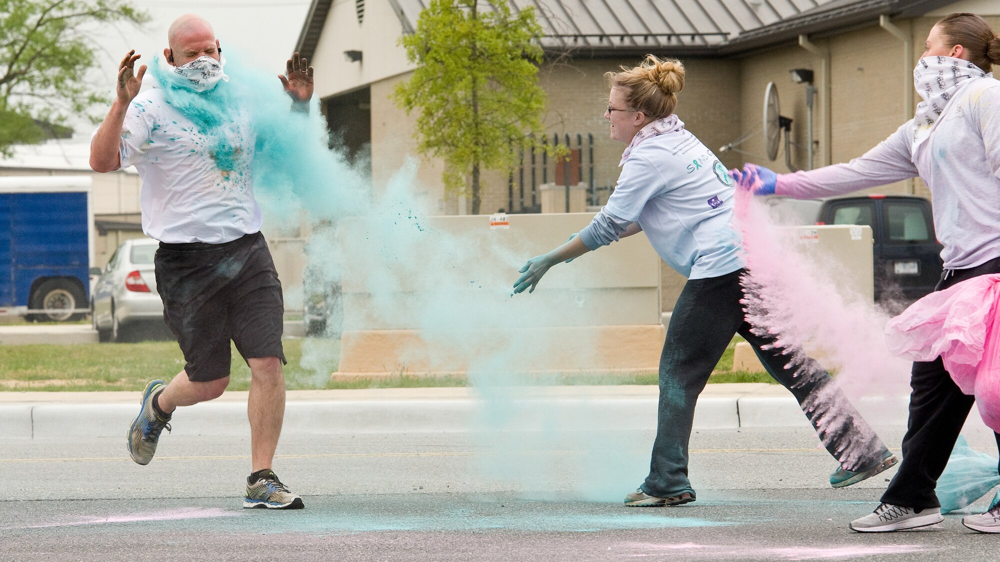 Senior Airmen Colleen Windsor, middle, and Jessica Casto, right, both from the 436th Logistics Readiness Squadron, course volunteers for the 5K Color Run, toss colored powder on Senior Master Sgt. Steven Ousley, 436th Aerial Port first sergeant, as he nears the finish line April 28, 2016, on Dover Air Force Base, Del. Volunteers dusted runners with colored powder at various course locations on base. (U.S. Air Force photo/Roland Balik)