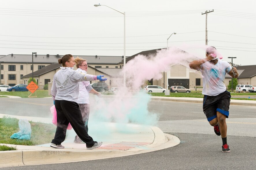 Course volunteers for the 5K Color Run, Senior Airmen Colleen Windsor, middle, and Jessica Casto, left, both from the 436th Logistics Readiness Squadron, toss colored powder on Senior Airman Yontaireus McCray, 436th Force Support Squadron, right, as he approaches the finish line April 28, 2016, on Dover Air Force Base, Del. Volunteers dusted runners with colored powder at various course locations on base. (U.S. Air Force photo/Roland Balik)