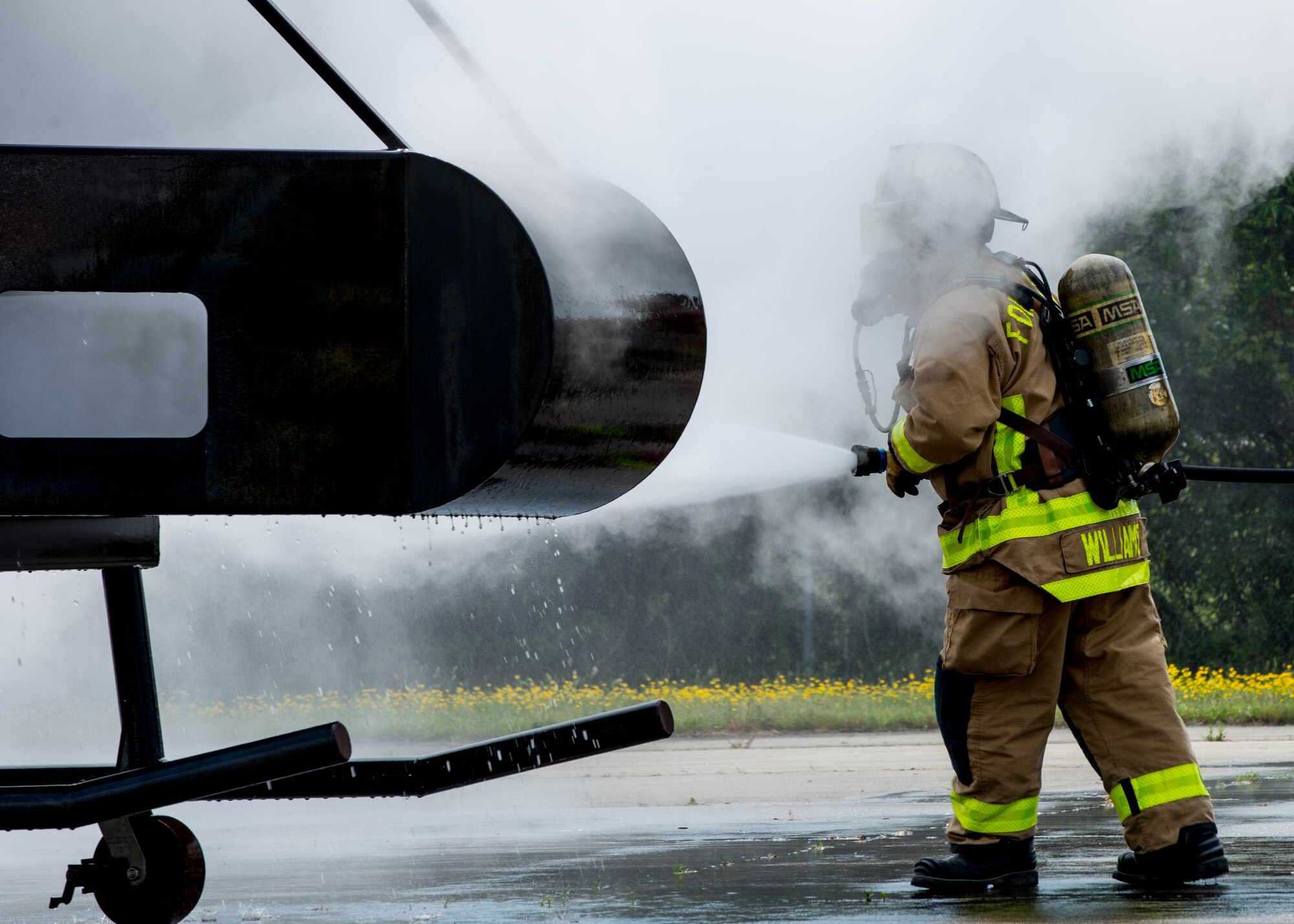 A Fort Eustis fire department fire fighter walks through smoke, extinguishing a fire during an aircraft live fire exercise at Fort Eustis, Va., April 27, 2016. The fire fighters practiced their approach to an aircraft emergency and practice proper turret procedures for rescue paths.  (U.S. Air Force photo by Staff Sgt. J.D. Strong II)
