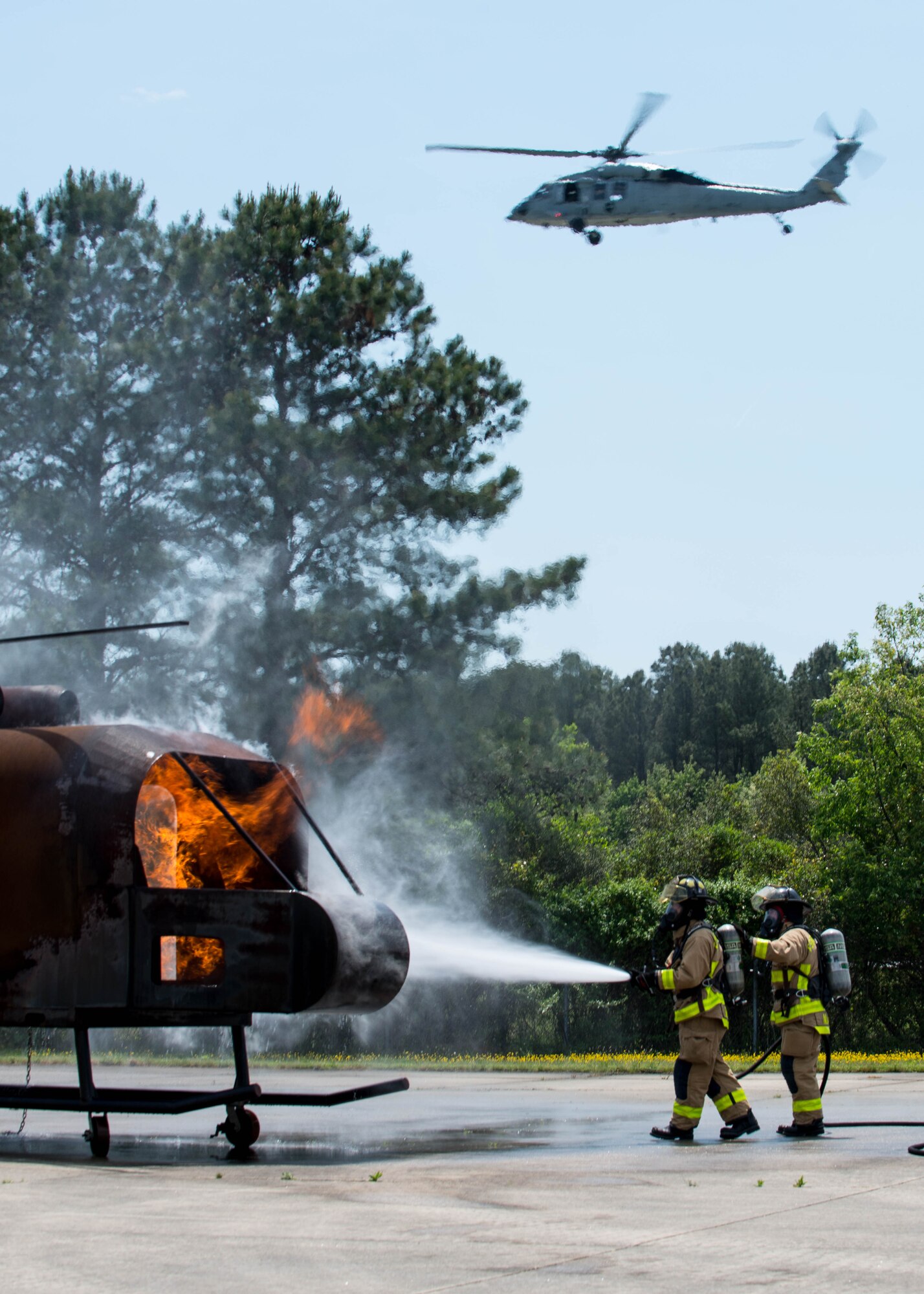 Fort Eustis fire department fire fighters extinguish a fire while a UH-60 Black Hawk flies overhead during an aircraft live fire exercise at Fort Eustis, Va., April 27, 2016. The majority of the Fort Eustis fire department’s aircraft responses are to helicopters. (U.S. Air Force photo by Staff Sgt. J.D. Strong II)