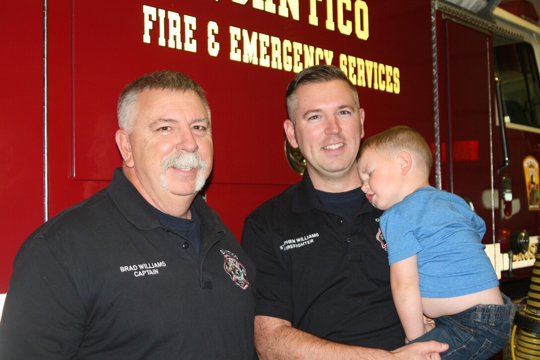 Capt. Brad Williams stands with his son, Firefighter Stephen Williams, and grandson Clint, 2, at Fire Station 533 on the west side of Marine Corps Base Quantico. Brad Williams will retire from Quantico Fire and Emergency Services Apr. 29 after 21 years and four months. Stephen Williams started work for the department in January. He hopes to retire from Quantico as well.