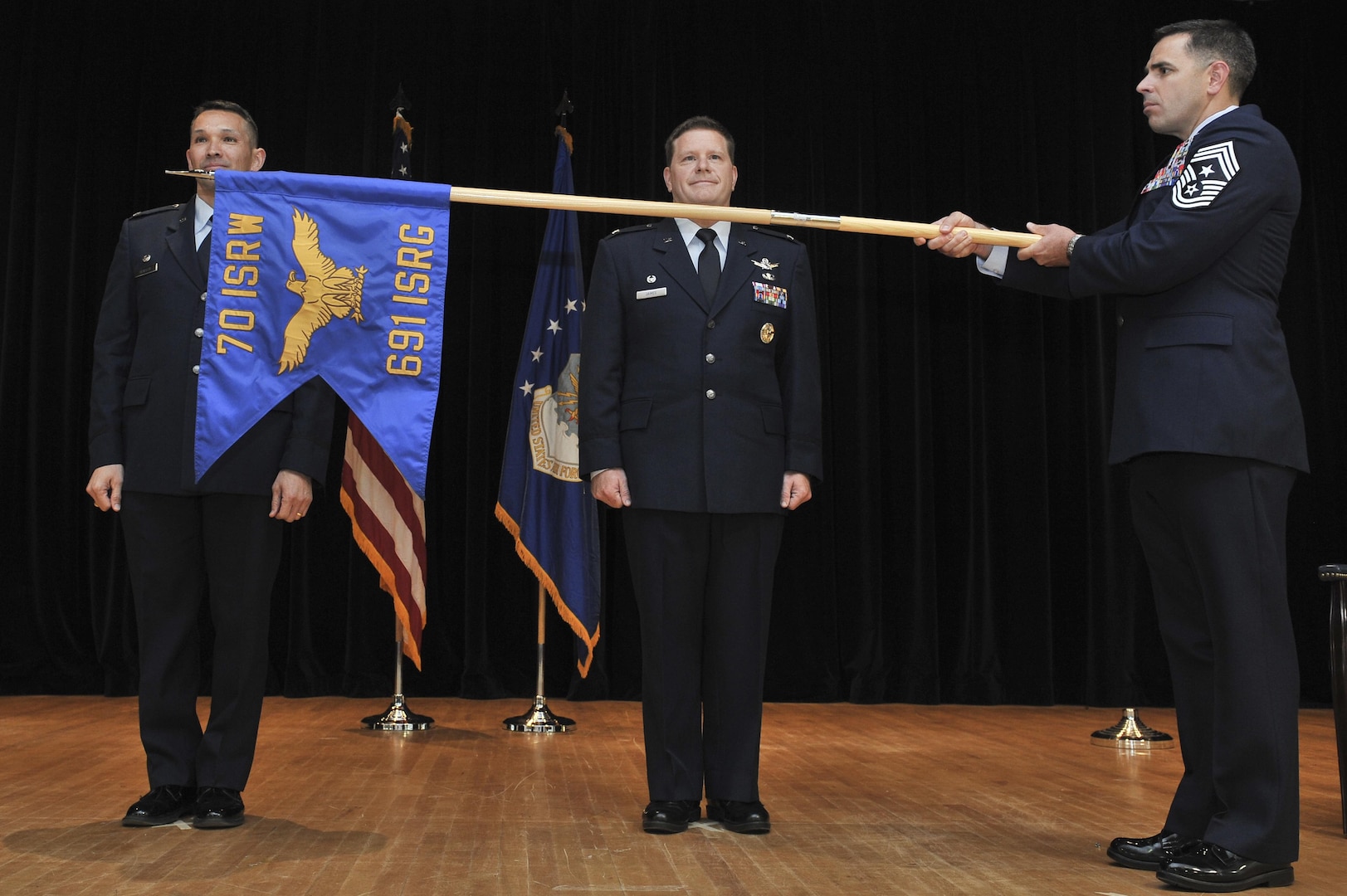 Colonel Thomas Hensley, 70th Intelligence, Surveillance and Reconnaissance Wing commander, and Col. David James, 691st ISRG commander, stand as Chief Master Sgt. Benjamin Higginbotham, 70th ISR Wing command chief, holds the unfurled 691st unit flag symbolizing the re-activation of the group May 5, 2016, at Fort George G. Meade, Md. Officially in-activated September 2014 at Royal Air Force Menwith Hill Station, United Kingdom, the 691st ISRG returns and is now activated under the 70th ISR Wing. (U.S. Air Force photo/Staff Sgt. Alexandre Montes)
