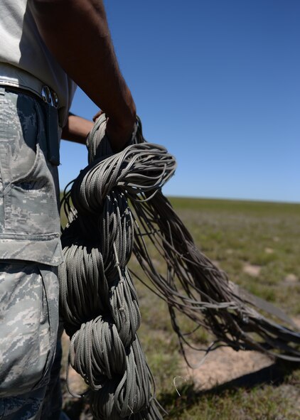 An Airman from the 97th Logistics Readiness Squadron shortens the paracord lines of a parachute after the cargo platforms were dropped from a U.S. Air Force C-17 Globemaster III cargo aircraft, May 4, 2016 Duke, Okla. Riggers build each platform used for loadmaster air drop training from the ground up, including packing the parachutes, securing the cargo, loading it into the aircraft and recovering it after it has landed. (U.S. Air Force photo by Senior Airman Nathan Clark/Released)
