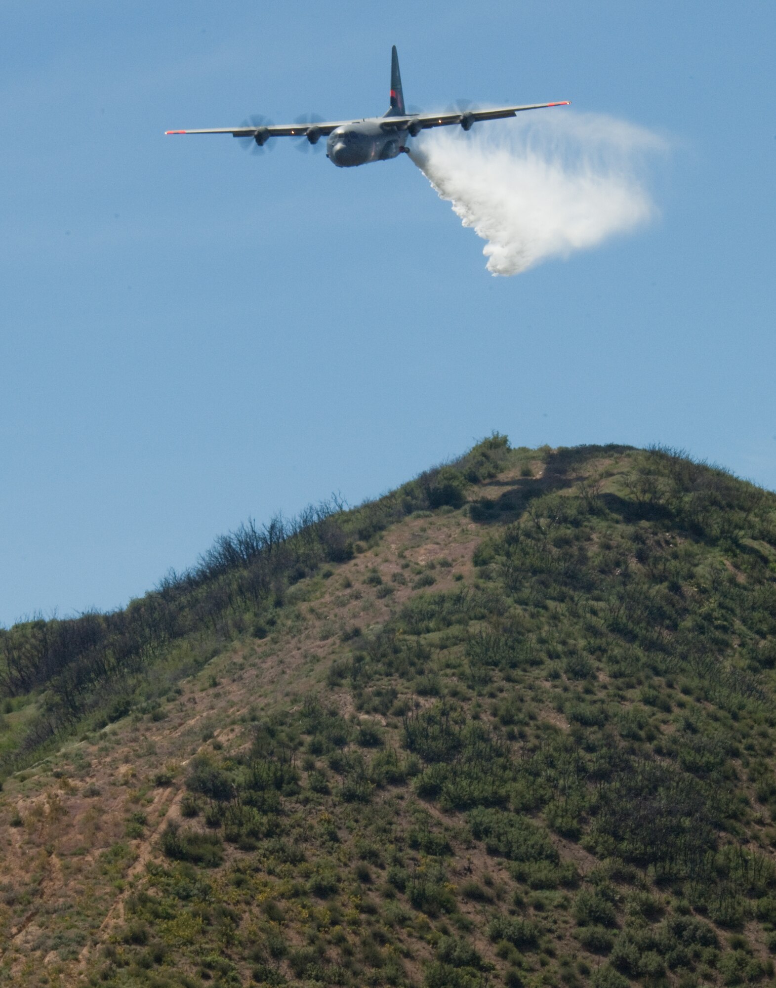 A line of water is dropped high above the Los Angeles Forest from a Air National Guard C-130 containing the MAFFS (Modular Airborne Firefighting System) system used to combat wildfires, during annual MAFFS training at the 146th Airlift Wing in Port Hueneme, California on May 3 2016. (U.S. Air National Guard photo by Staff Sgt. Nicholas Carzis) 