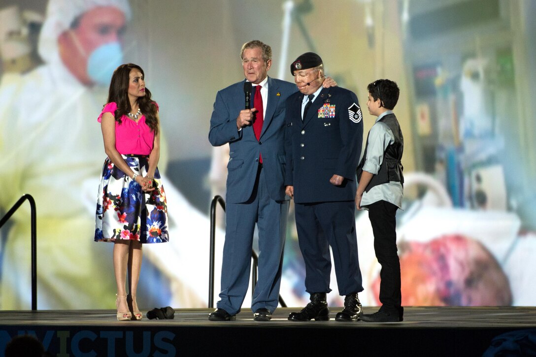 Former President George W. Bush speaks with Air Force Master Sgt. Israel Del Toro and his family during the opening ceremony for the 2016 Invictus Games in Orlando, Fla., May 8, 2016. A large photo of Bush visiting Del Toro in the hospital hangs in the background. DoD photo by EJ Hersom