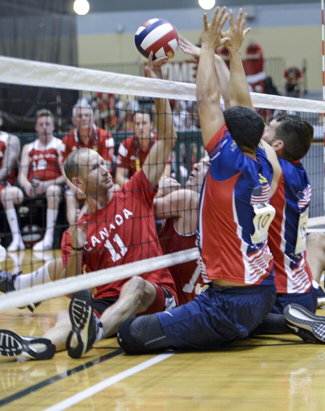 Two U.S. team athletes, right, block a serve against the Canadian team in a sitting volleyball match at the 2016 Invictus Games in Orlando, Fla., May 7, 2016. Air Force photo by Senior Master Sgt. Kevin Wallace