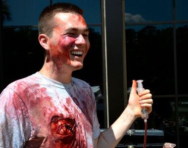 U.S. Air Force Senior Airman Paul Boyd, 628th Medical Support Squadron, biomedical equipment technician, laughs as he tests a fake blood dispenser during the 2016 LowCountry Skills Fair, May 4, 2016, at Joint Base Charleston - Naval Weapons Station, S.C. Role players were outfitted with moulage to simulate patients with medical illnesses for competitors to practice on during the fair. (U.S. Air Force photo by Staff Sgt. Michael Battles)