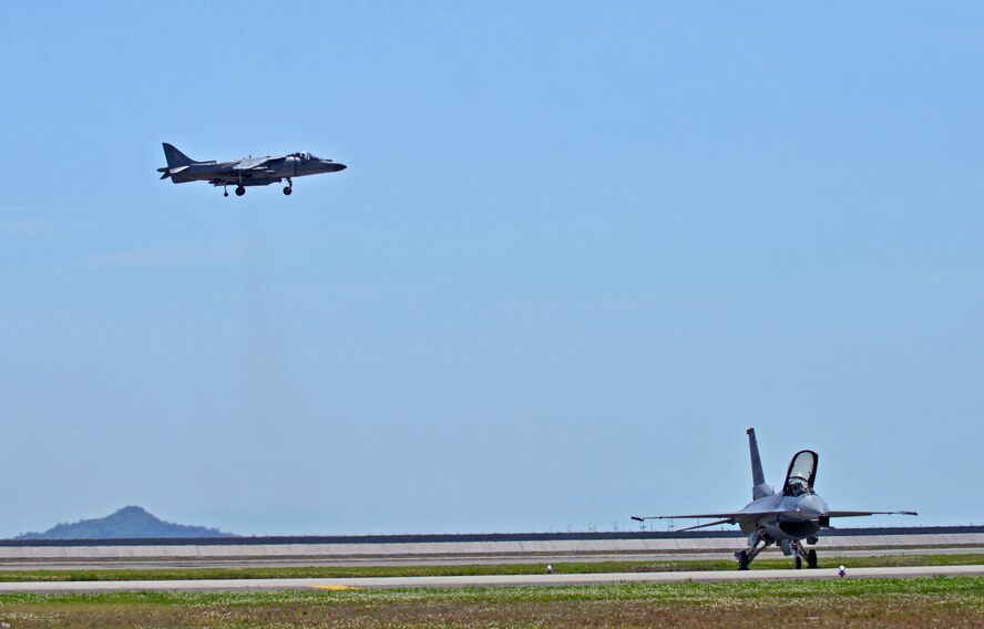An AV-8B Harrier II hovers in the air beside an F-16 Fighting Falcon on the flightline during the 2016 Friendship Day at Marine Corps Air Station Iwakuni, Japan, May 5, 2016. Since 1973, MCAS Iwakuni has conducted a single-day air show and open house specifically designed to foster positive relationships between the air station and Japan. (U.S. Air Force photo by Senior Airman David Owsianka/Released)
