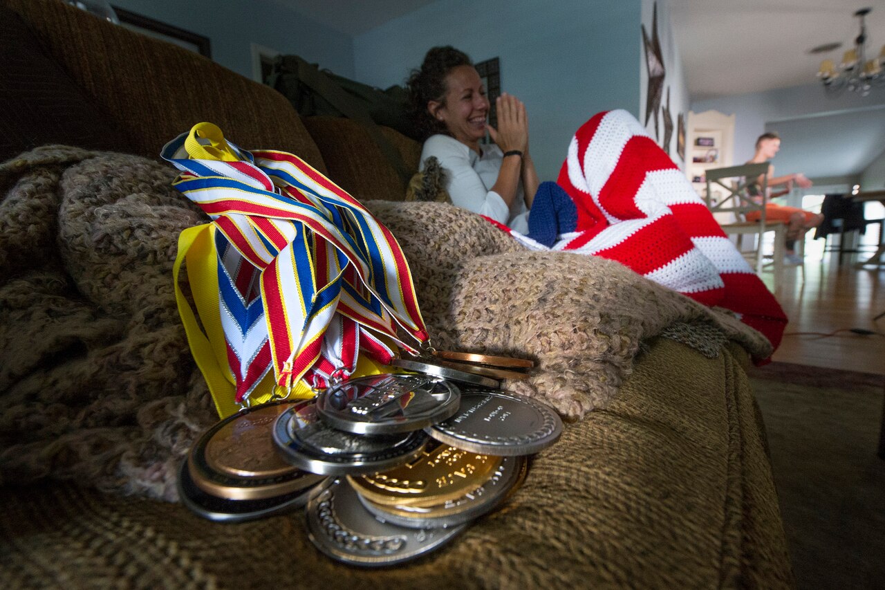 Army Capt. Kelly Elmlinger reacts to a story being told about her by her best friend, Aaron Stewart, at Elmlinger’s home in San Antonio, June 10, 2015. In the foreground are medals Elmlinger has earned in adaptive sports. DoD photo by EJ Hersom