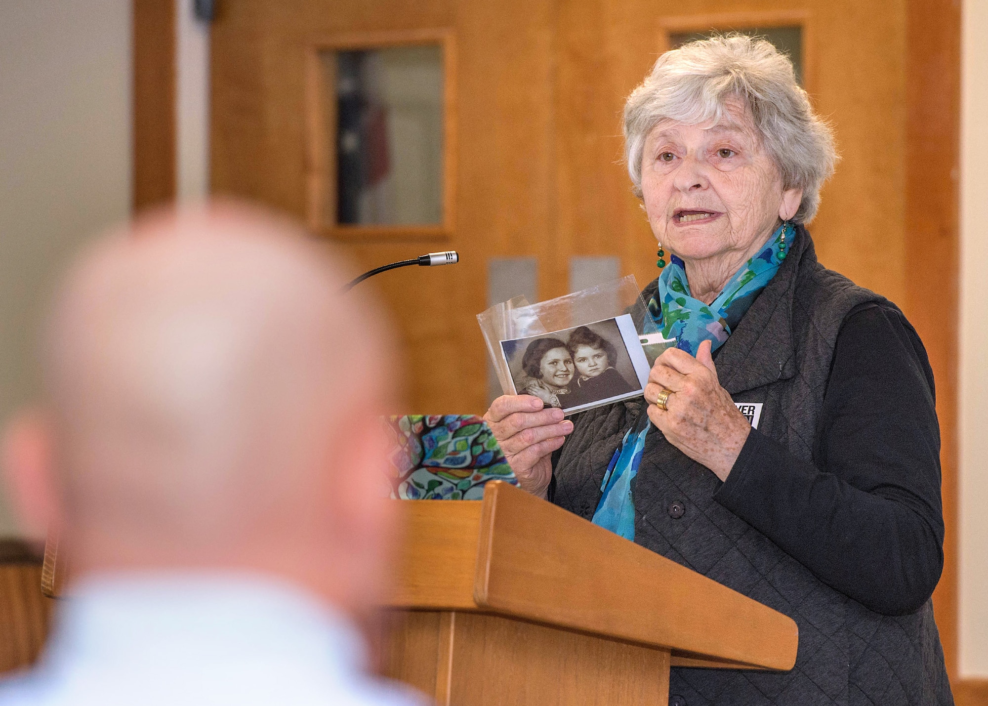 Eva Paddock, Holocaust and Kindertransport survivor, holds up a picture of her sister, Milena, and her as children during a Holocaust Remembrance Week observances at the base chapel May 5. Paddock discussed how her and other children were granted safe passage to Great Britain by Nazi Germany as part of Kindertransport from 1938 to 1940. (U.S. Air Force photo by Jerry Saslav)