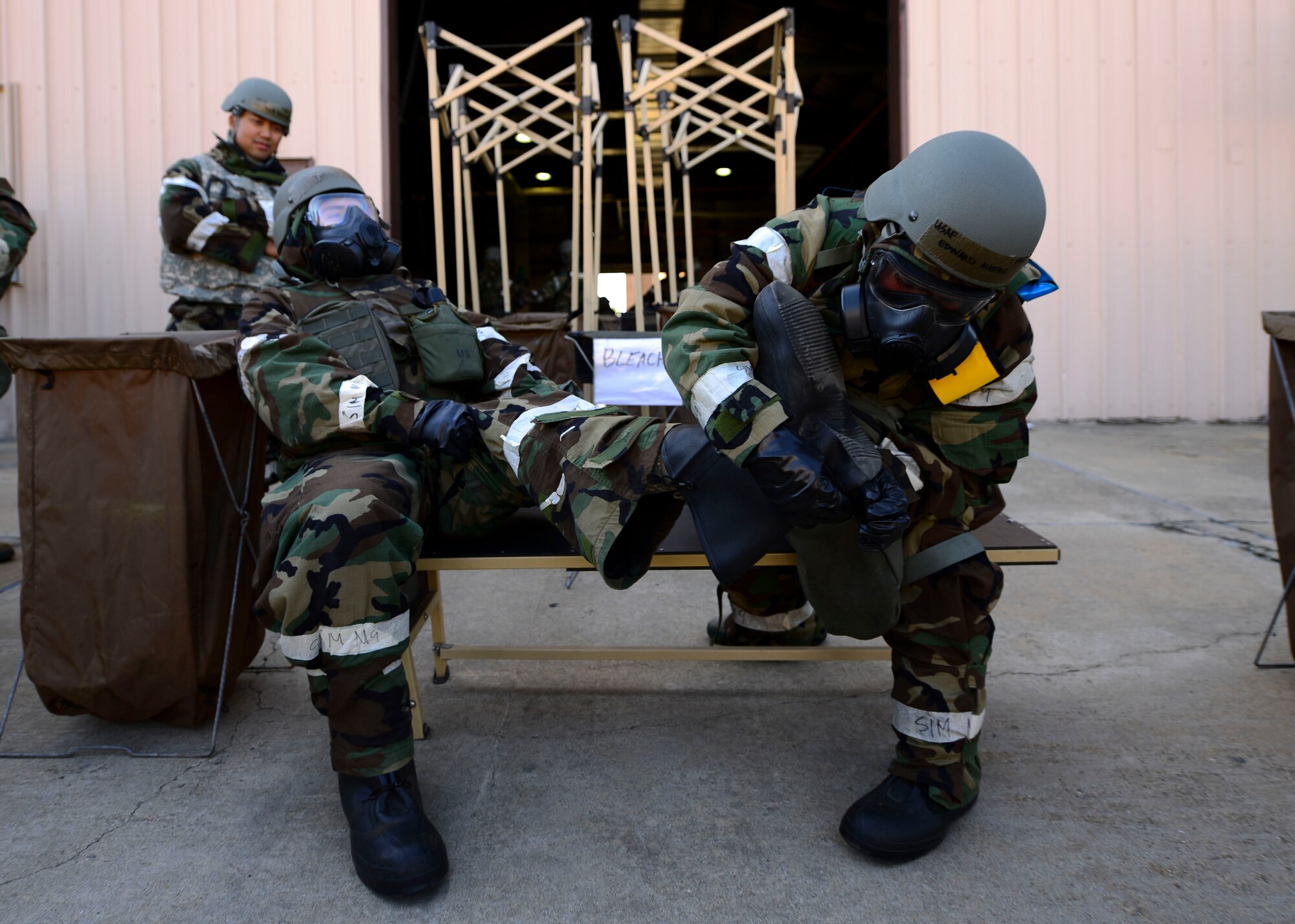 Airmen from the 51st Civil Engineer Squadron take off their Mission Oriented Protective Posture boots while going through a mock-decontamination line at Osan Air Base, Republic of Korea, May 11, 2016. The 51st CES held a training event during Exercise Beverly Herd 16-01 to give CES Airmen a chance to practice wartime survival skills. (U.S. Air Force photo by Senior Airman Victor J. Caputo/Released)