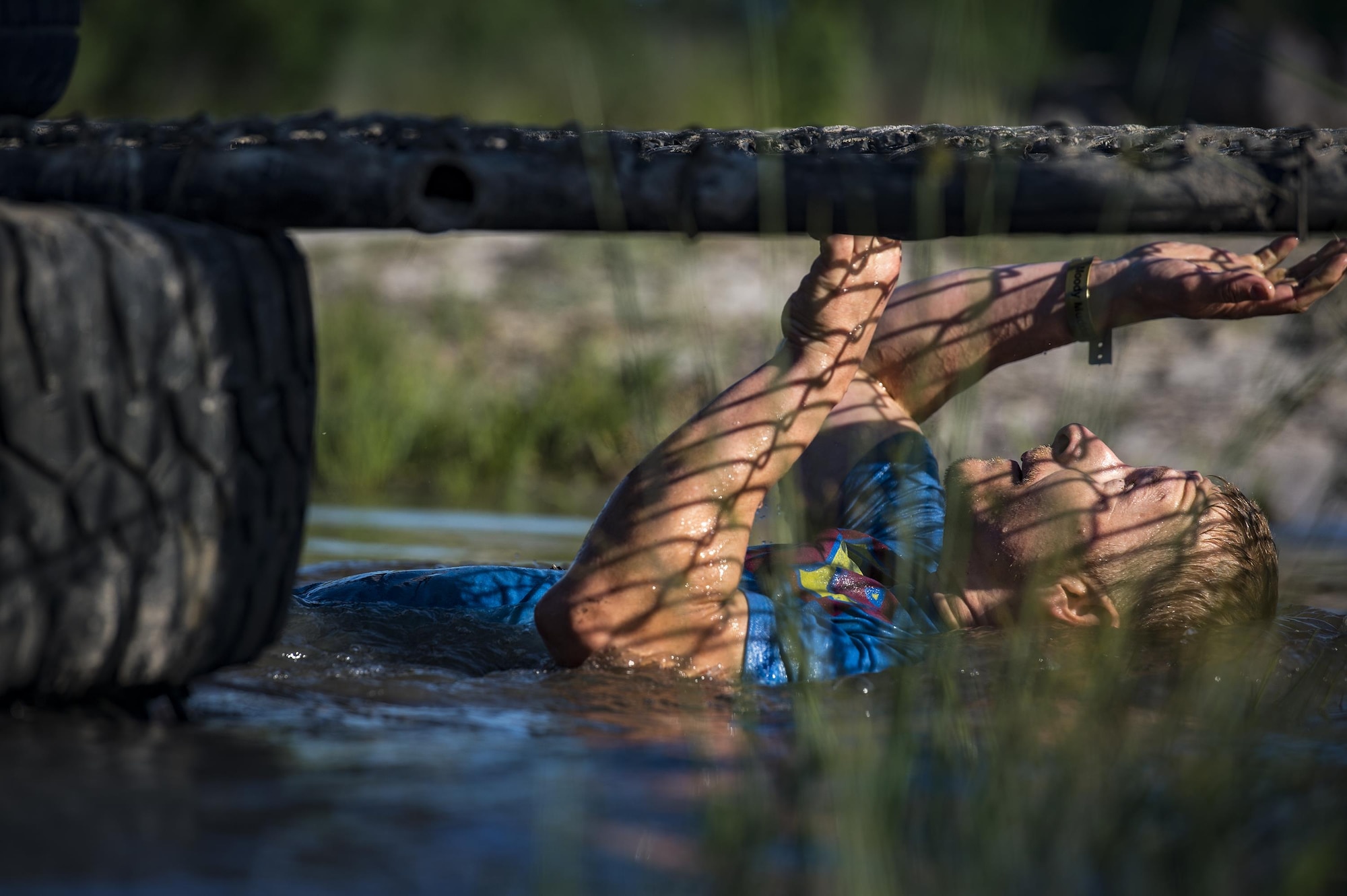 A runner pulls himself under a section of chain-link fence during the 2016 Moody Mudder, May 7, 2016, in Ray City, Ga. The Mudder challenged nearly 500 competitors to complete 20 obstacles on a 3.12-mile course for the third year in a row.  (U.S. Air Force photo by Senior Airman Ryan Callaghan/Released)