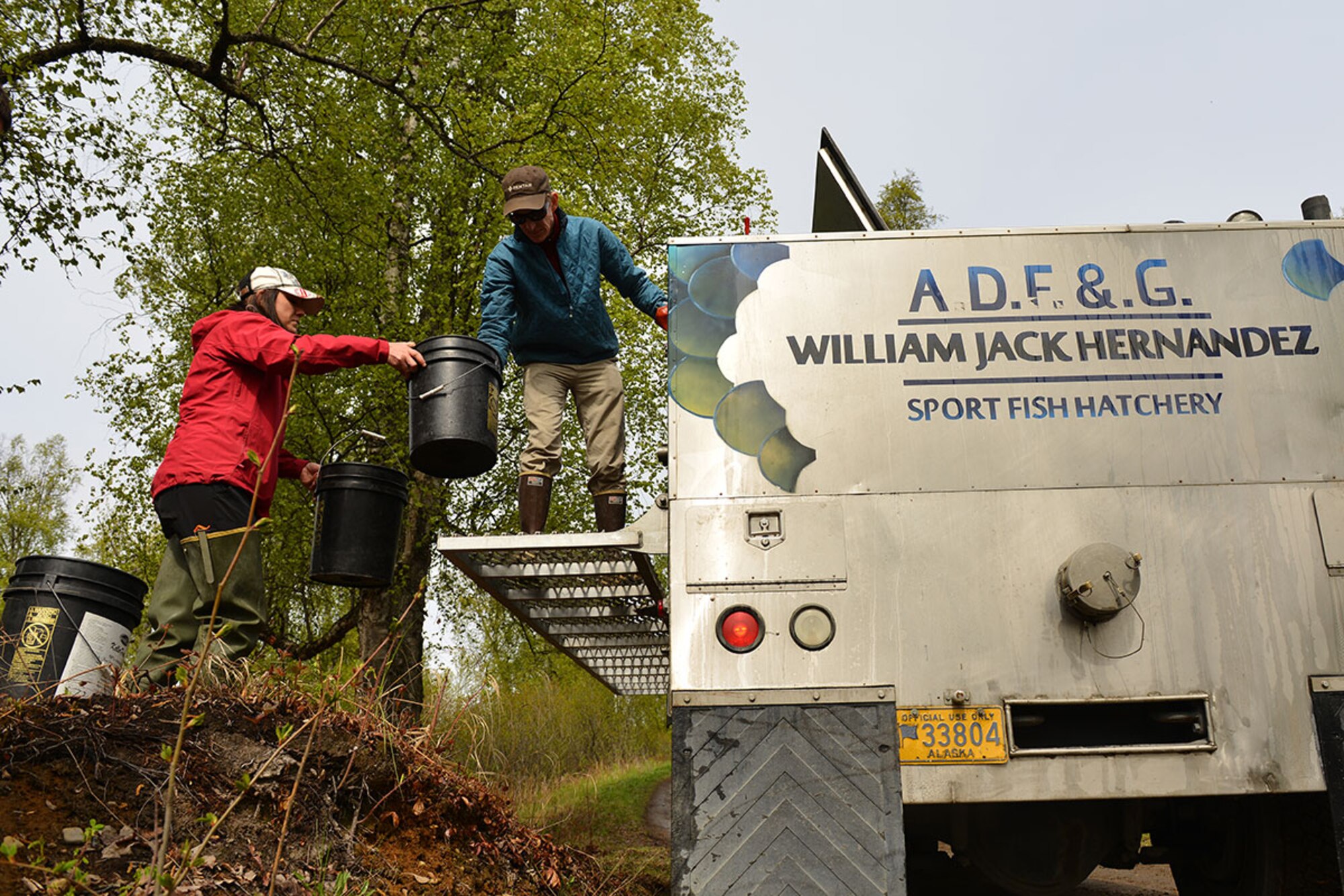 Krystina Bottom, fisheries crew lead with the Center for Environmental Management of Military Lands takes two buckets of rainbow trout from Chuck Pratt, a fish culturist from the William Jack Hernandez Sport Fish Hatchery on the bank of Fish Lake May 9. the fish are transported from the hatchery to lakes all around the area and even go as far as Seward, Alaska. (U.S. Air Force photo by Senior Airman Kyle Johnson)