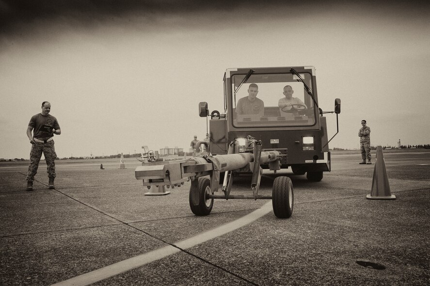 Airmen with the 730 Air Mobility Squadron work together to drive an aircraft tow vehicle during a challenge for the 730 AMS Maintenance Rodeo at Yokota Air Base, Japan, May 6, 2016. Six teams participated in the rodeo which had a variety of challenges: tool box inventory, safety wire skill, vehicle tow bar push, power cart relay race and Mission Oriented Protective Postures (MOPP) gear and Self Aid Buddy Care (SABC) timed event. (U.S. Air Force photo by Yasuo Osakabe/Released)