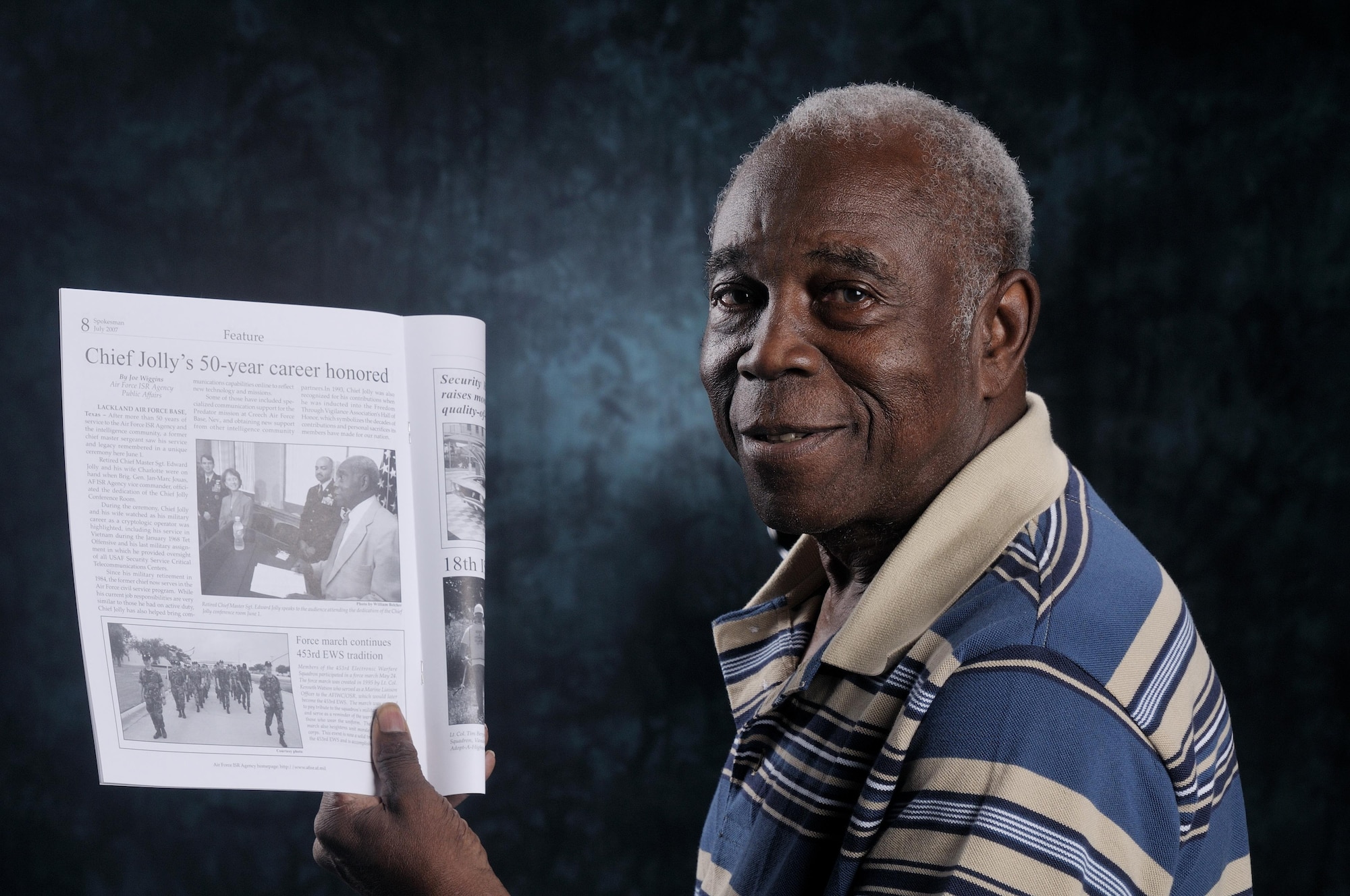 Mr. Edward Jolly, Jr, CMSgt, retired, 75, of the Air Force Intelligence, Surveillance and Reconnaissance Agency, A6, holds a Spokesman magazine showing an article depicting Jolly's 50 years of service, both military and civilian.  The AF ISR Agency/A6 Conference Room now bears his name.