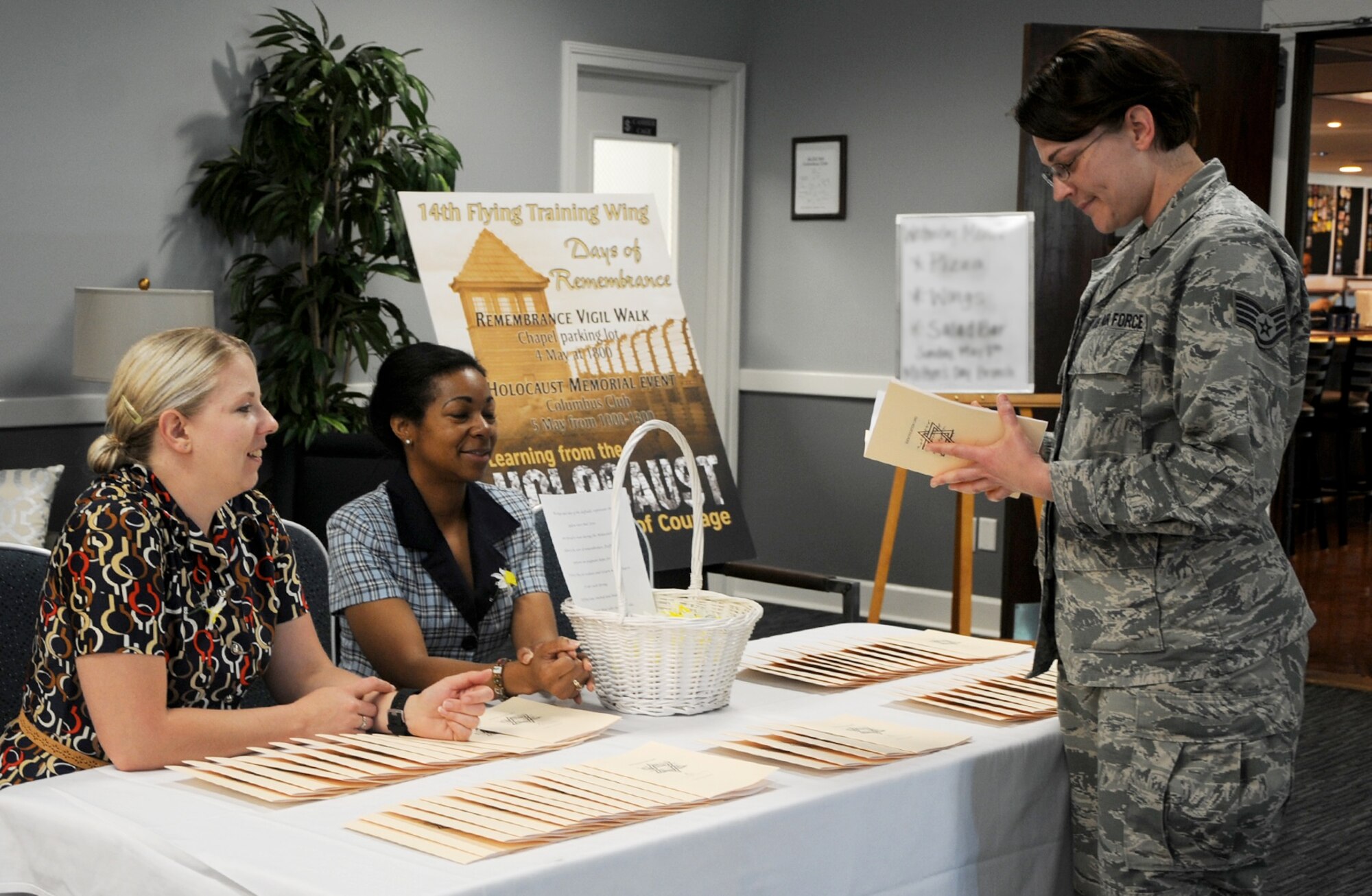 Tech. Sgt. Stephanie Reynard and Master Sgt. Carmina Beedle, Holocaust Memorial volunteers, hand information to Staff Sgt. Maria Schinella, 14th Medical Operations Squadron, and other attendees during the museum event May 5 at Columbus Air Force Base, Mississippi. Attendees were shown the history of events while touring around the Columbus Club and were even treated to an educational video projected in the event room. (U.S. Air Force photo/Melissa Doublin)
