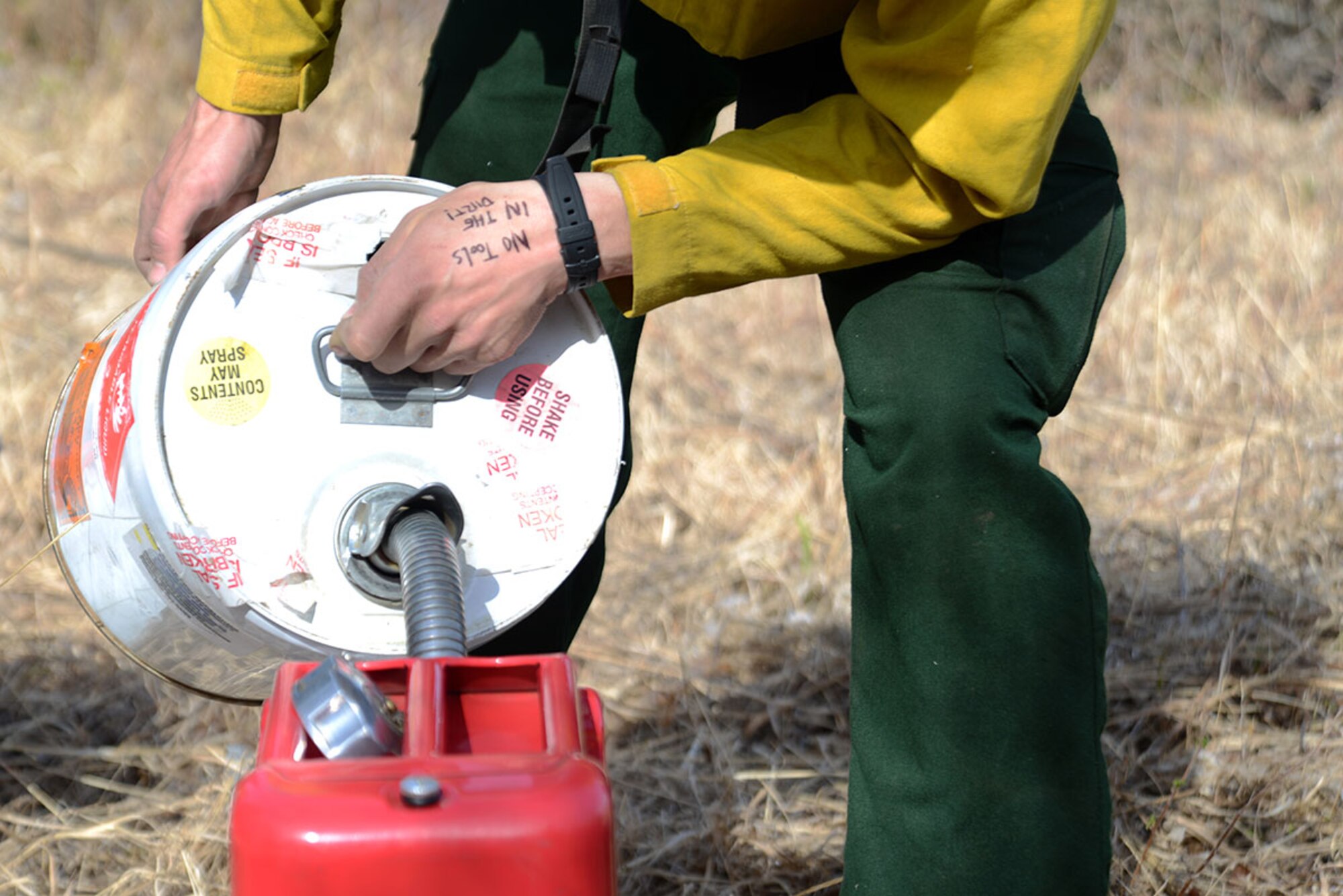 A crewmember with the Alaska Division of Forestry fills a fuel canister with gasoline to power the portable fire pump hose. A portable fire pump hose was one of the methods available to extinguish flames outside of the designated burn perimeter. (U.S. Air Force photo by Airman 1st Class Christopher R. Morales)