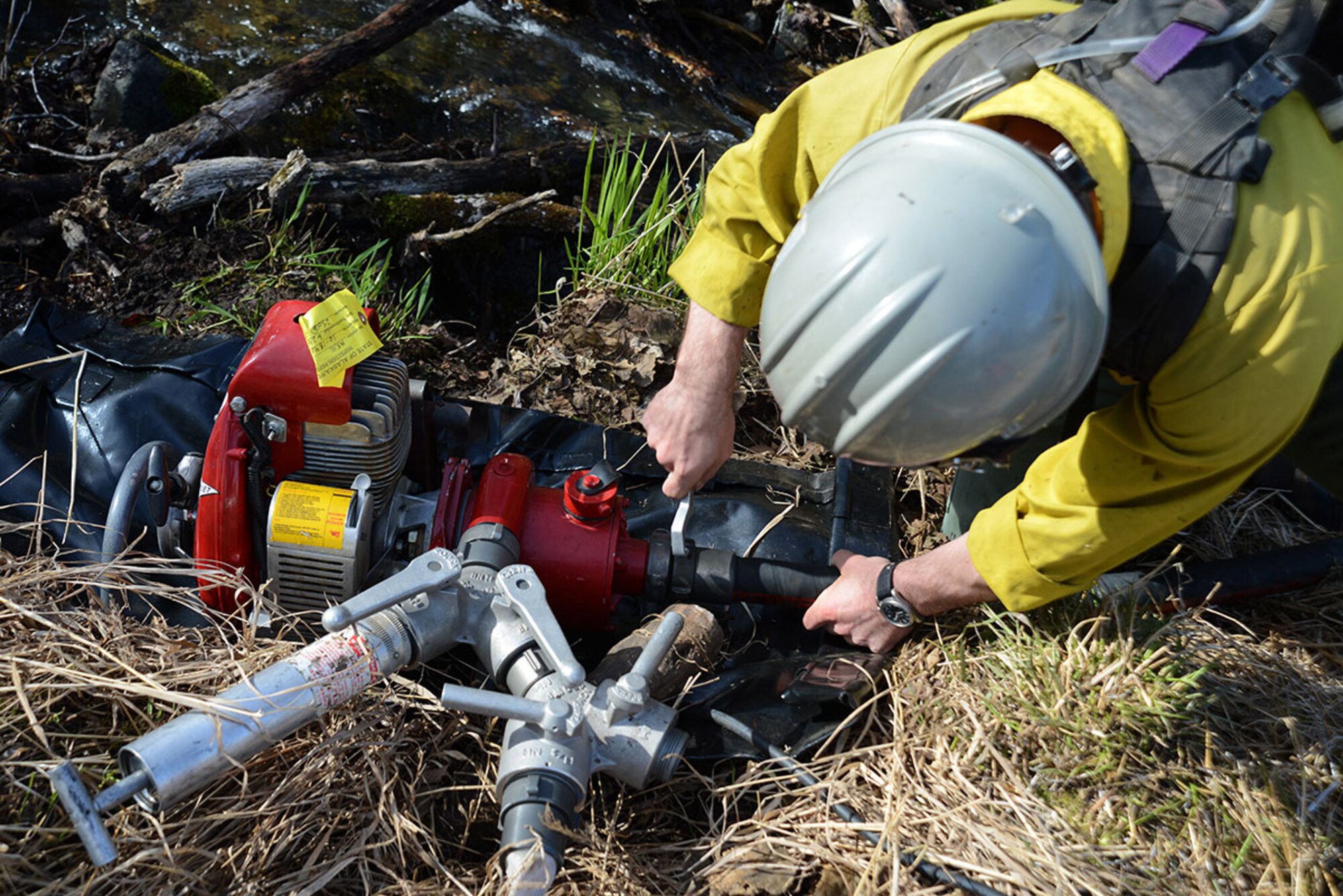 A crewmember with the Alaska Division of Forestry attaches a suction hose drawing water from a small river to a portable fire pump hose at Grezelka range, Alaska, May 2, 2016. A portable fire pump hose was one of the methods available to extinguish flames outside of the designated burn perimeter. (U.S. Air Force photo by Airman 1st Class Christopher R. Morales)