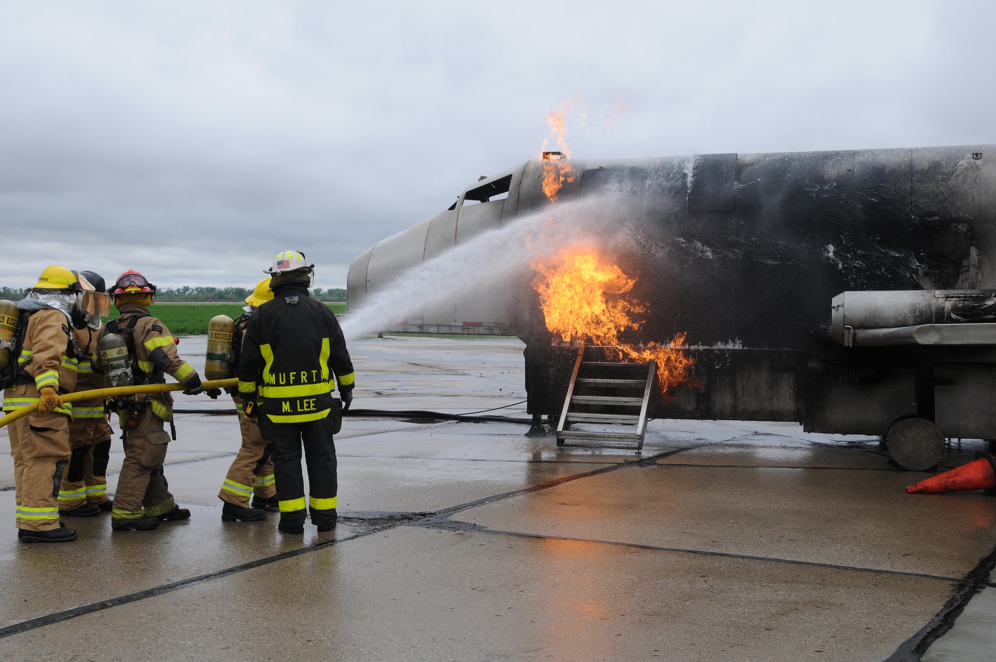 Fireman hose down flames coming from the cabin door of a Mobile Aircraft Rescue Firefighter Trainer, while a MARFT instructor looks on, during a training exercise at the Sioux City Airport on May 11, 2016. The training is part of a joint exercise between Firefighters from the 185th Air Refueling Wing, Fire Emergency Services and Sioux City Fire and Rescue. (U.S. Air National Guard photo by: Staff Sgt. David Asbra/Released)