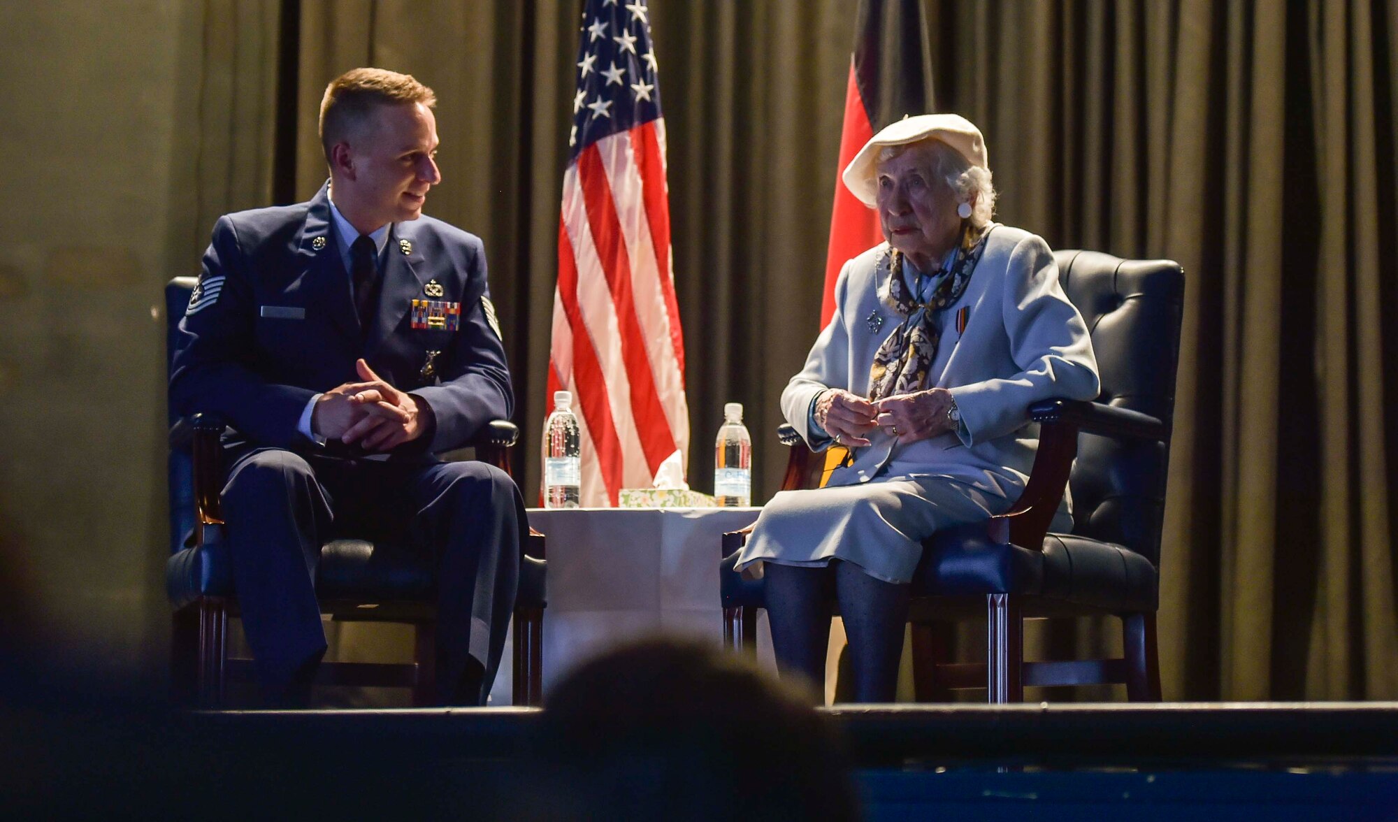 Ms. Selma Van de Perre, 92-year-old Holocaust survivor, sits with Tech Sgt. Robert Jarvis, 86th Civil Engineer Squadron fire fighter, during a Holocaust remembrance event held at Ramstein Air Base, Germany May 6, 2016. Van de Perre shared her story of surviving Ravensbrück, a women’s concentration camp. (U.S. Air Force photo/Tech Sgt. Sara Keller) 