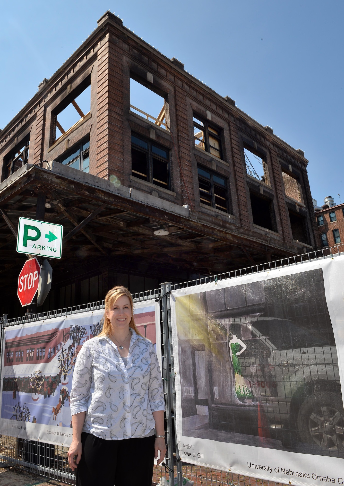 Lisa Gill, with the 55th Force Support Squadron, stands next to her banner art that surround the Mercer Building in Omaha’s Old Market, May 5, 2016.  Lisa was one of two artists from Offutt Air Force Base selected to have their work displayed on the construction fence that surrounds the downtown renovation of the Mercer Building after a fire destroyed much of the century-old building.  (U.S. Air Force photo by Josh Plueger/Released)