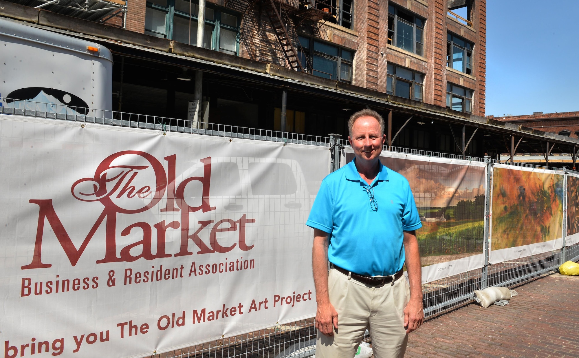 Ken Smith, a weather operations requirements manager with to the 557th Weather Wing, stands at the beginning of the Old Market Business Association’s beautification project on Howard Street in downtown Omaha, Neb., May 5, 2016.  Smith was one of 37 artists selected to have their work displayed along the construction, barrier fence that will help shield the renovation efforts from the local downtown attractions.  (U.S. Air Force photo by Josh Plueger/Released)