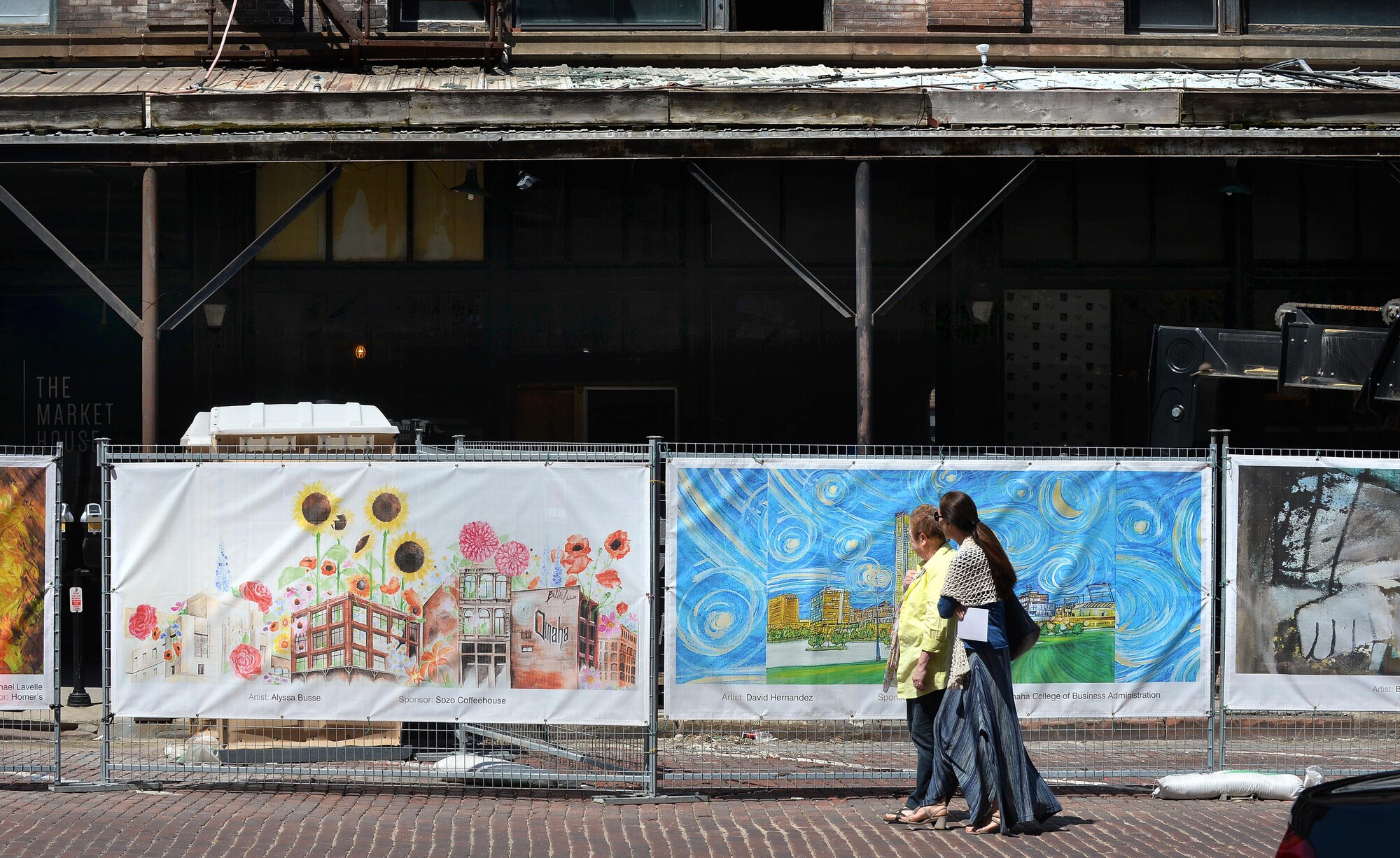 Old Market pedestrians walk by the Old Market Business Association’s beautification project on Howard Street in downtown Omaha, Neb., May 5, 2016.  The fence that runs along the corner of Howard and 11th Street surrounds the construction site of the Mercer Building which almost burned down in January.  The fence displays 37, selected pieces of art from Omaha-area artists to help beautify the intersection during the renovation.  (U.S. Air Force photo by Josh Plueger/Released)