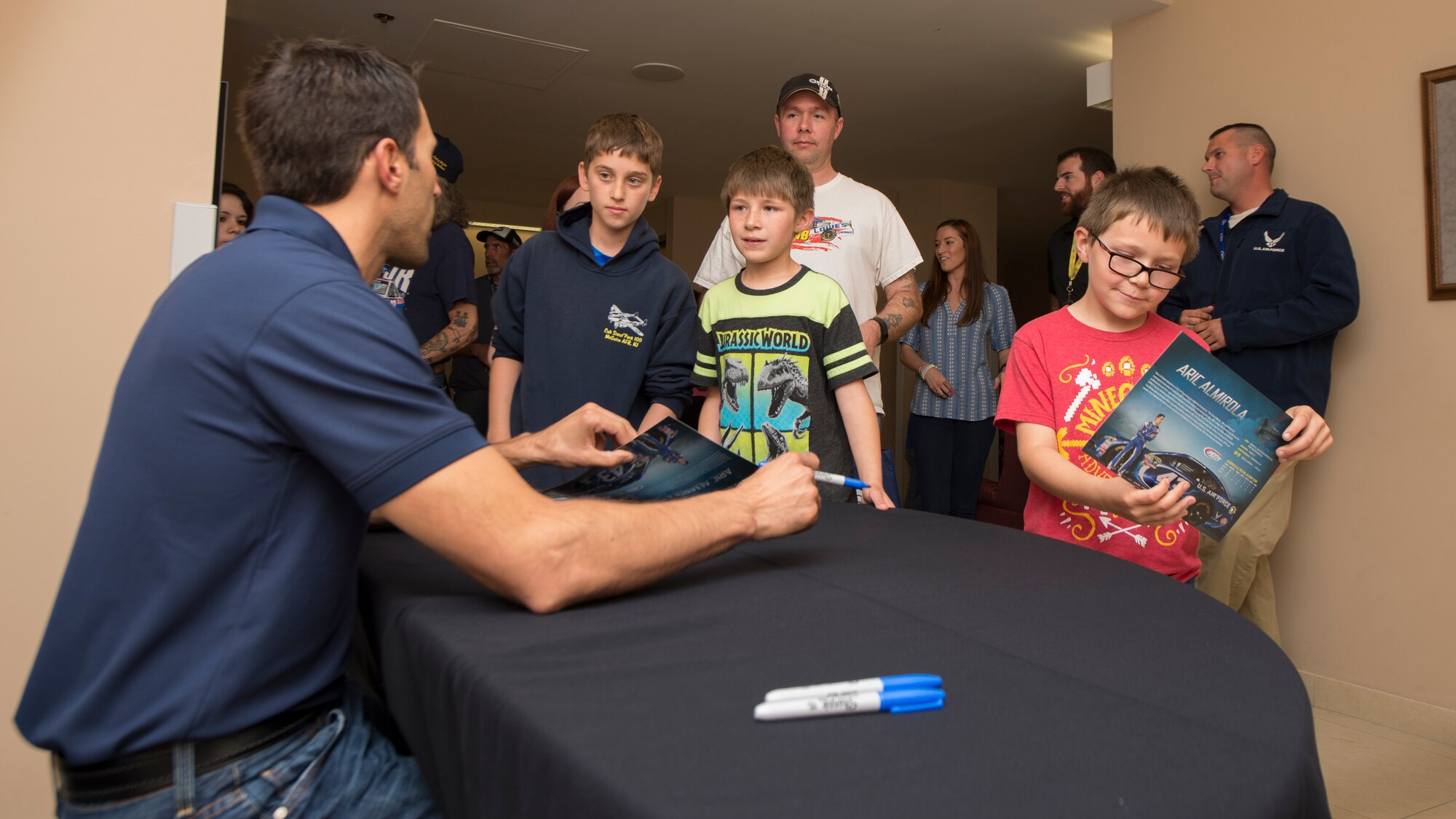 Aric Almirola, driver of the No. 43 U.S. Air Force Ford Fusion, signs autographs and meets with Tech. Sgt. Jerry Ivey, 436th Airlift Wing Command Post senior emergency action controller, and his sons at the Dover Air Force Base Race Weekend Social at the Landings on Dover AFB, Del. Almirola’s NASCAR stock car is partially sponsored by the U.S. Air Force. (U.S. Air Force photo/Senior Airman Zachary Cacicia)