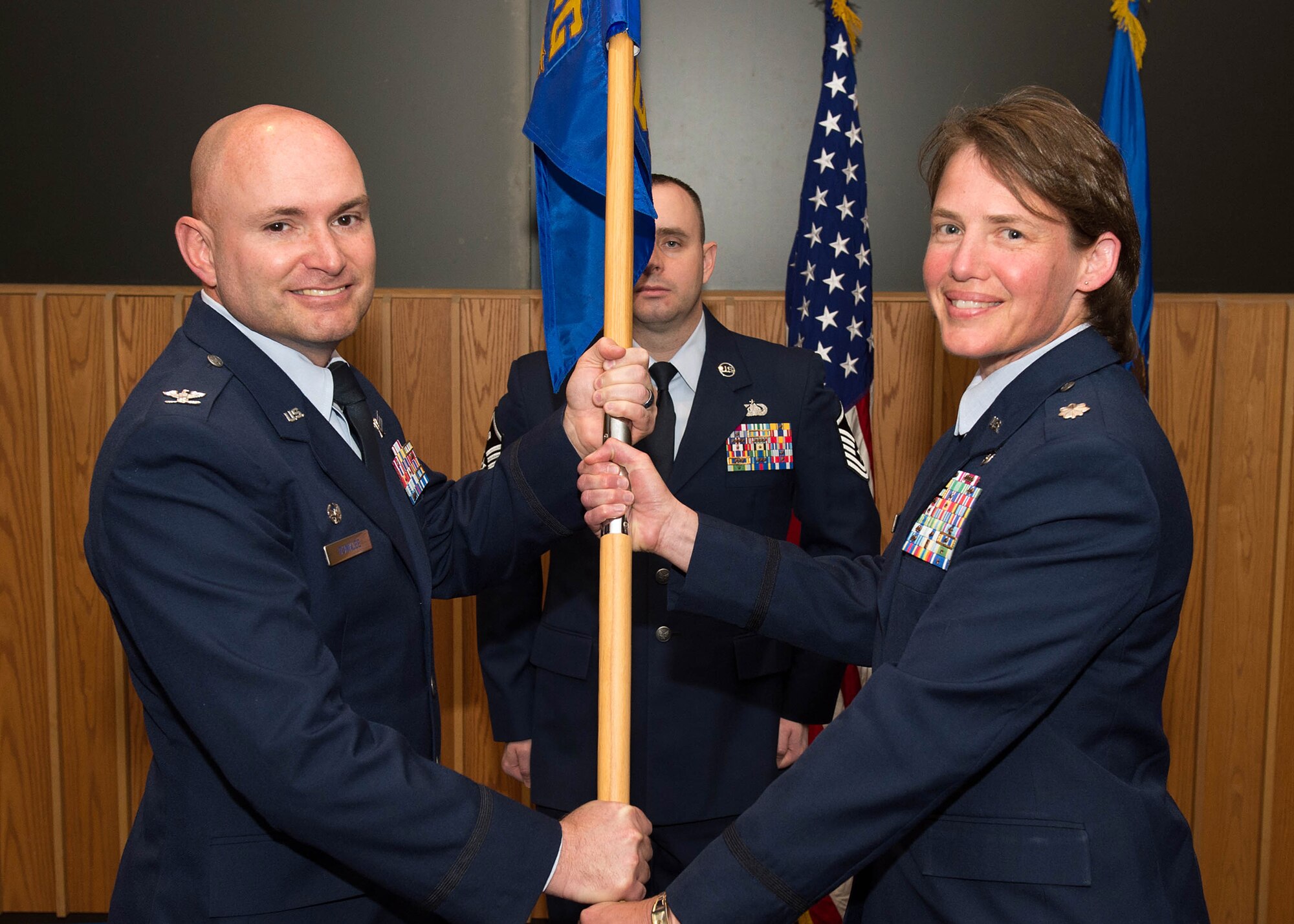 Col. David R. Dunklee, 66th Air Base Group commander, passes the 66th Medical Squadron guidon to Lt. Col. Lynn M. Shinabery during a change of command ceremony at the O'Neill Auditorium on base May 12, while Master Sgt. Jason Oliver, 66 MDS first sergeant, looks on. As commander of Hanscom's Medical Treatment Facility, Shinabery is responsible for the daily operations of 157 personnel and a 125,000 beneficiary population. (U.S. Air Force photo by Jerry Saslav)