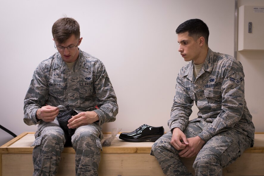 (Left) Senior Airman Michael Natalello, Yokota Honor Guard equipment custodian and assistant flight trainer, shows Airman 1st Class Robert Gamboa, Yokota Honor Guard, how to attach horseshoe heel clickers to a pair of low quarters during honor guard training at Yokota Air Base, Japan, May 11, 2016. The idea of the heel clickers is to make only one audible click when every member steps to signify a unified movement. (U.S. Air Force photo by Staff Sgt. Michael Washburn/Released)