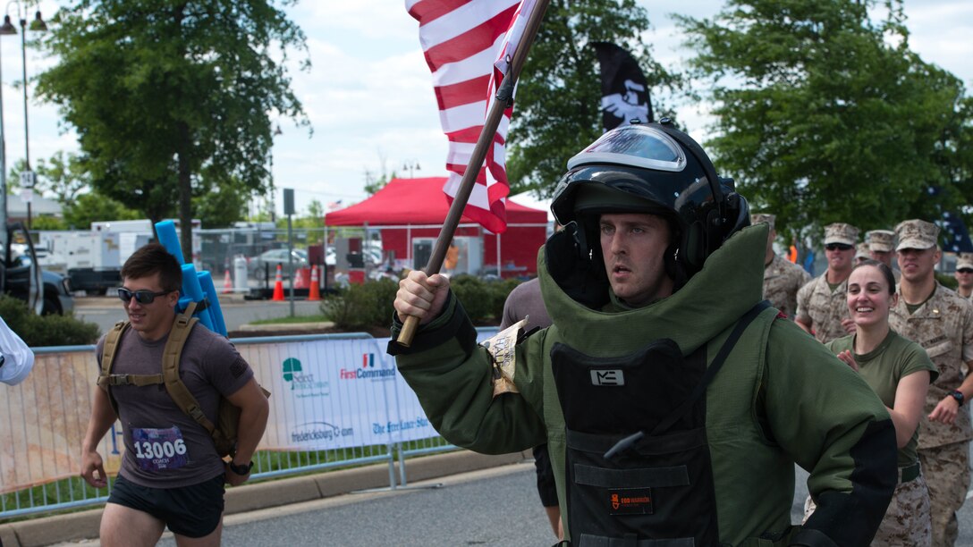Navy Lt. Daniel Glenn runs with the American flag at the Marine Corps Historic Half Marathon in Fredericksburg, Virginia, May 15, 2016. Despite being exhausted and in pain from his 85 pound bomb suit, Glenn, with a large group of Marines at his back, charged the final leg of the course to complete the half marathon. 