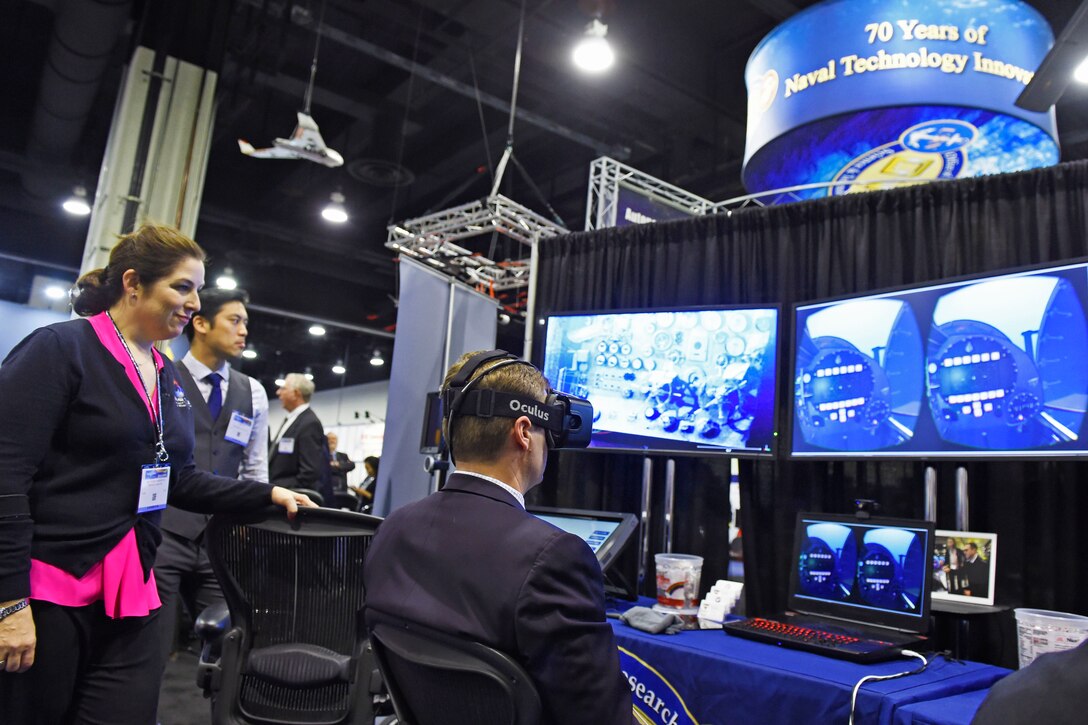 Space and Naval Warfare Systems Command Systems Center Pacific's Lauren Burnette explains the Battlespace Exploitation of Mixed Reality Lab demo to a visitor at the Office of Naval Research exhibit during the 2016 Sea-Air-Space Exposition at National Harbor, Md., May 16, 2016. Navy photo by John F. Williams