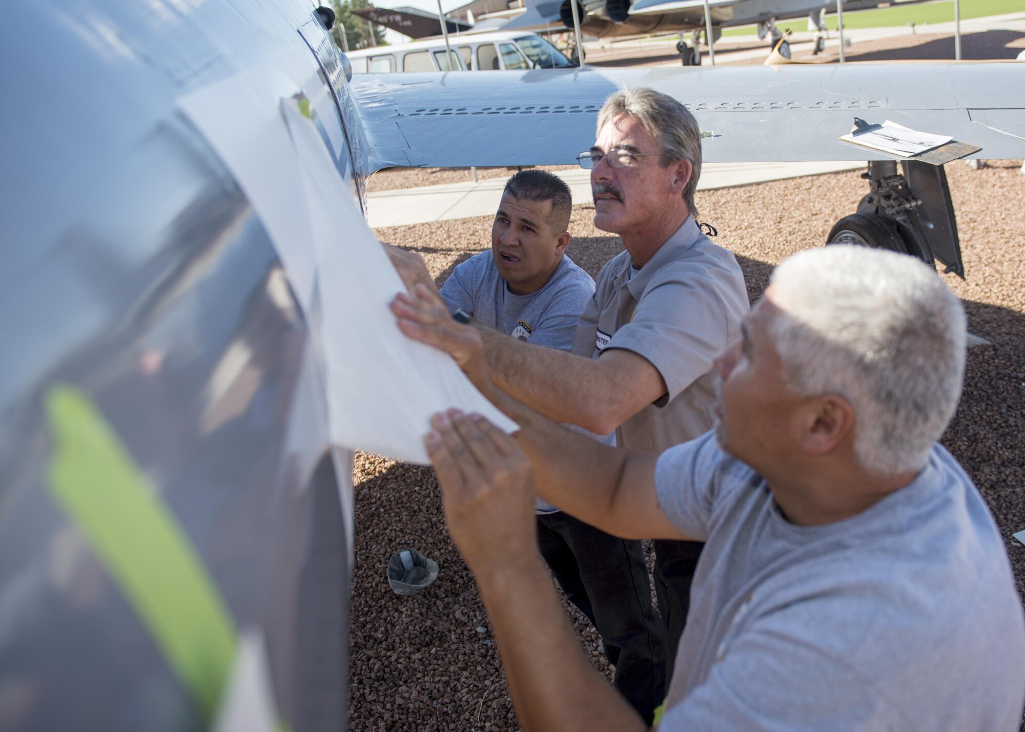 From left to right: Jesse, Mike, and Frank, M1 Support Systems aircraft corrosion specialists at Holloman Air Force Base N.M., pull of the outer sheet of a decal to an F-84F Thunderstreak at Heritage Park here May 16. These contractors sand and re-paint two aircraft inside Heritage Park each year to keep them from corroding. (Last names are being withheld do to operational requirements) (U.S. Air Force photo by Airman 1st Class Randahl J. Jenson) 