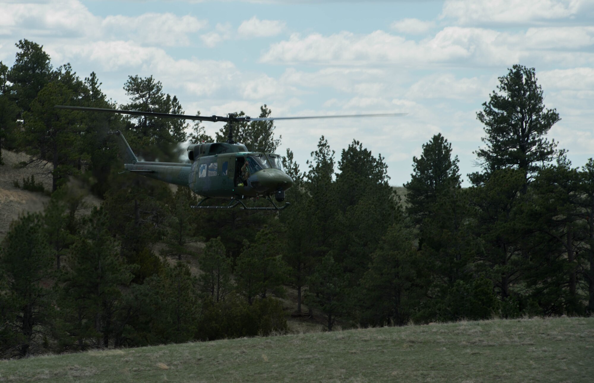 A UH-1 Huey helicopter circles overhead to patrol the area and look for the opposing forces during exercise Road Warrior at Camp Guernsey, Wyo., May 3, 2016. The 621st CRW Airmen played the opposing force for the Global Strike Command exercise, which evaluates tactics, techniques, and procedures used to secure nuclear–capable weapons and critical intercontinental ballistic missile components during convoy operations. (U.S. Air Force photo by Staff Sgt. Robert Hicks/Released)