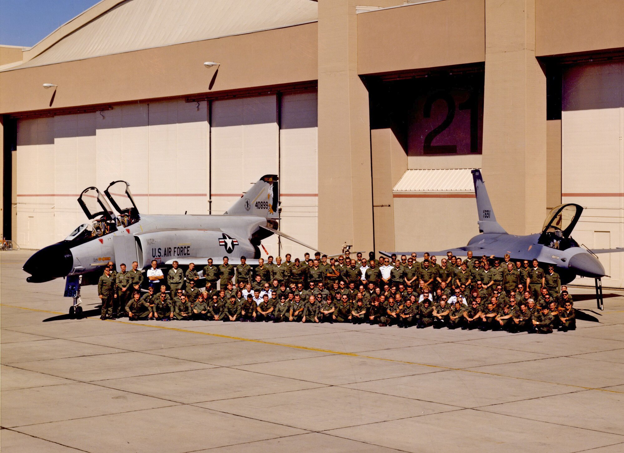 Members of the 114th Tactical Training Fighter Squadron pose for a group photo in front of an F-4 Phantom and an F-16 Falcon, both bearing the distinct Kingsley tail flash.  In 1989, the F-4 Schoolhouse converted to an F-16 training mission as the Air Force transitioned the alert mission to the F-16 Falcon.  (U.S, Air National Guard file photo) 
