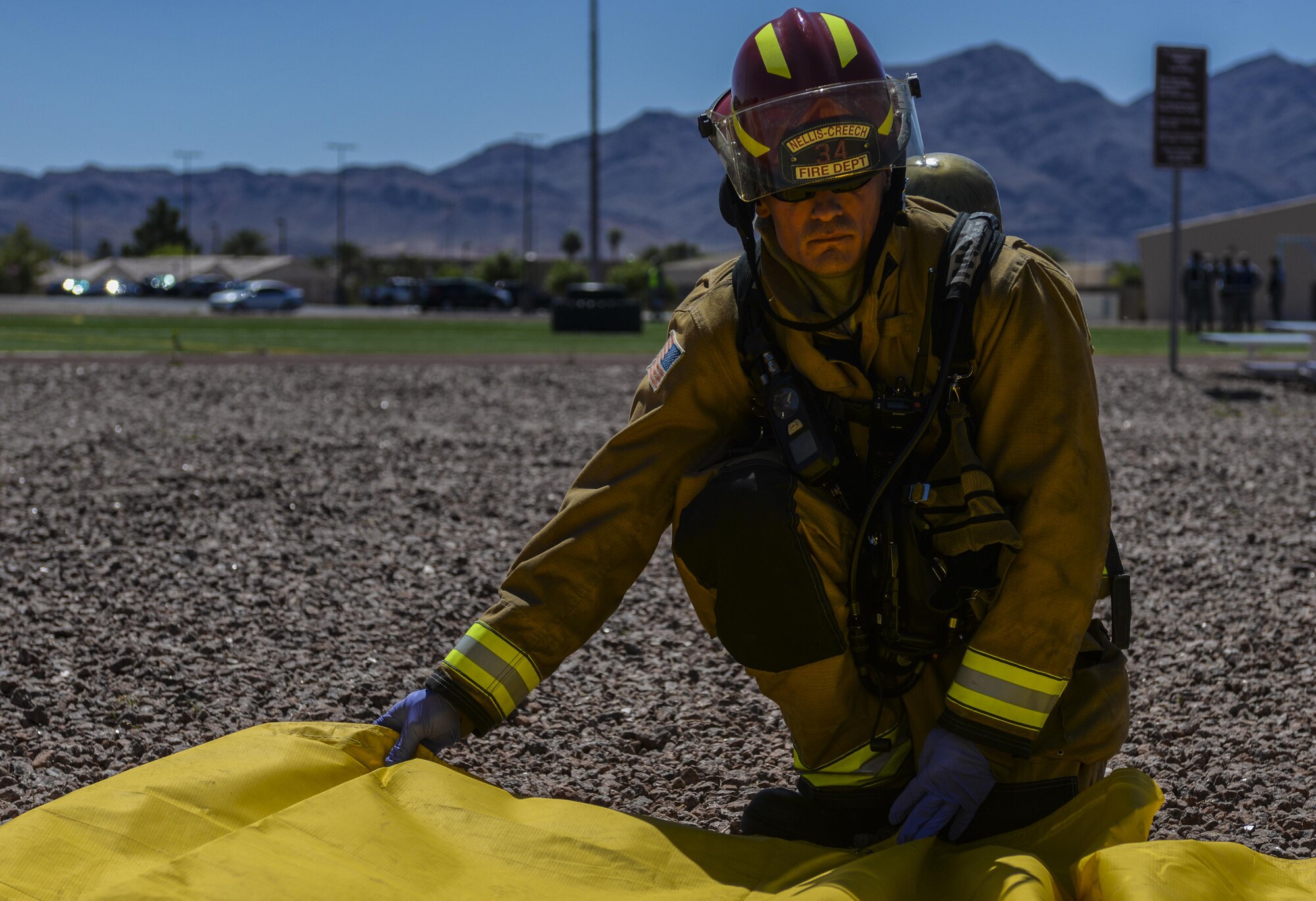 A 99th Civil Engineer Squadron Fire Protection Flight Airman spreads open a yellow triage tarp during a base exercise at Nellis Air Force Base, Nev., May 12, 2016. The simulated attacks occurred at the track at the Warrior Fitness Center during a mock squadron PT and at Hangar 220 during a mock ceremony. (U.S. Air Force photo by Airman 1st Class Kevin Tanenbaum)