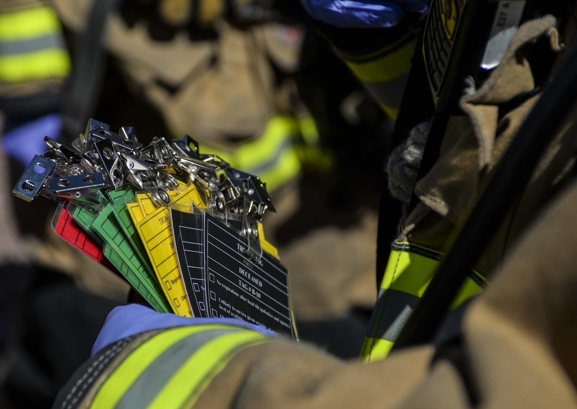 A 99th Civil Engineer Squadron Fire Protection Flight Airman passes out triage tags to label the severity of simulated injuries during a base exercise at Nellis Air Force Base, Nev., May 12, 2016. Each scenario had simulated active shooters and included volunteers who underwent moulage to simulate injuries that would occur during such an attack. (U.S. Air Force photo by Airman 1st Class Kevin Tanenbaum)