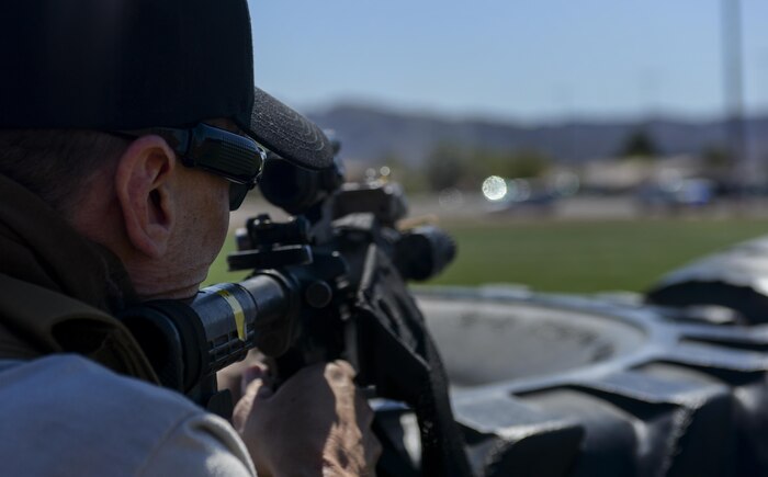 A simulated active shooter aims down the sights of an M-4 loaded with blanks as the first 99th Security Forces Squadron truck pulls up to the scene during a base wide exercise at Nellis Air Force Base, Nev., May 12, 2016. The simulated attacks occurred at the track at the Warrior Fitness Center during a mock squadron PT and at Hangar 220 during a mock ceremony. (U.S. Air Force photo by Airman 1st Class Kevin Tanenbaum)