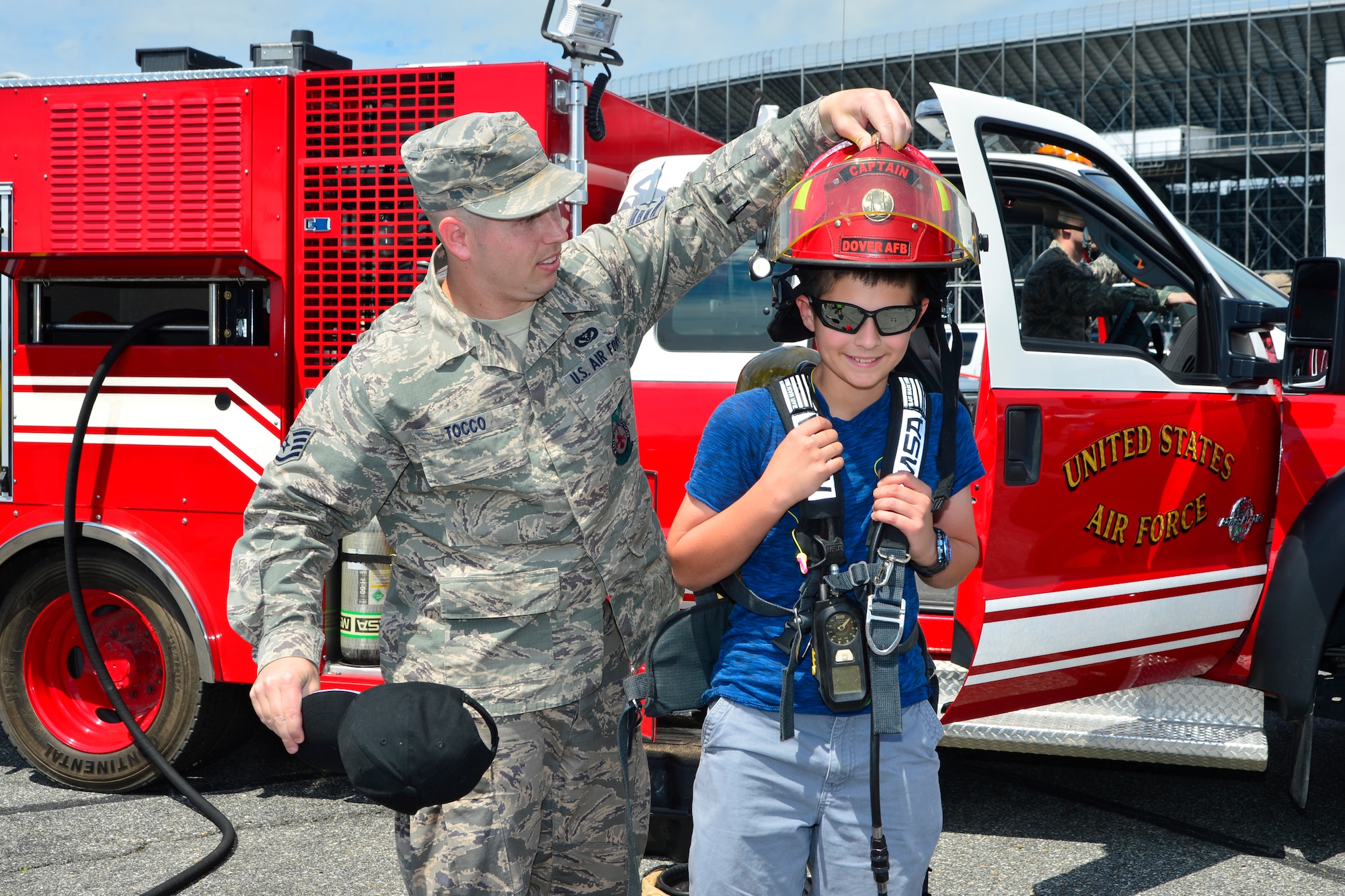 Staff Sgt. Aaron Tocco, 436th Civil Engineer Squadron firefighter, places a helmet on Jacob Richard inside the Monster Mile Youth Nation May 14, 2016, at Dover International Speedway in Dover, Del. Team Dover Airmen volunteered over the race weekend to let fans interact with Airmen and mission equipment. (U.S. Air Force photo/Senior Airman William Johnson)