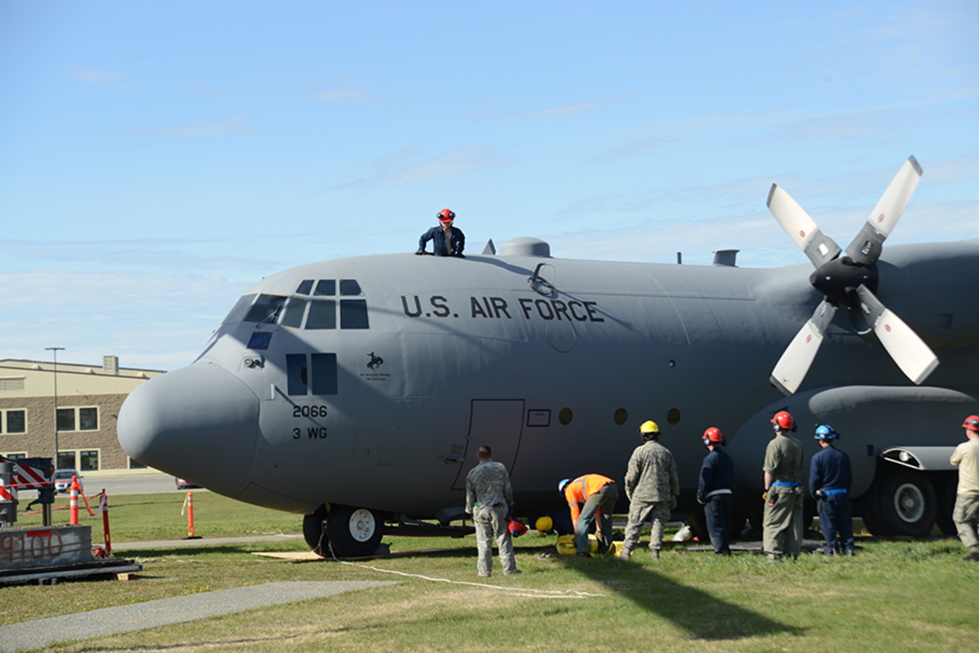 A 3rd Maintenance Squadron Airman peers down from a C-130 Hercules to help place lift straps, necessary to lift the aircraft onto a pedestal at Heritage Park at Joint Base Elmendorf-Richardson, Alaska, May 12, 2016. Lift straps were placed at key points to distribute more than 17,000 pounds of weight equally. (U.S. Air Force photo by Airman 1st Class Christopher R. Morales)