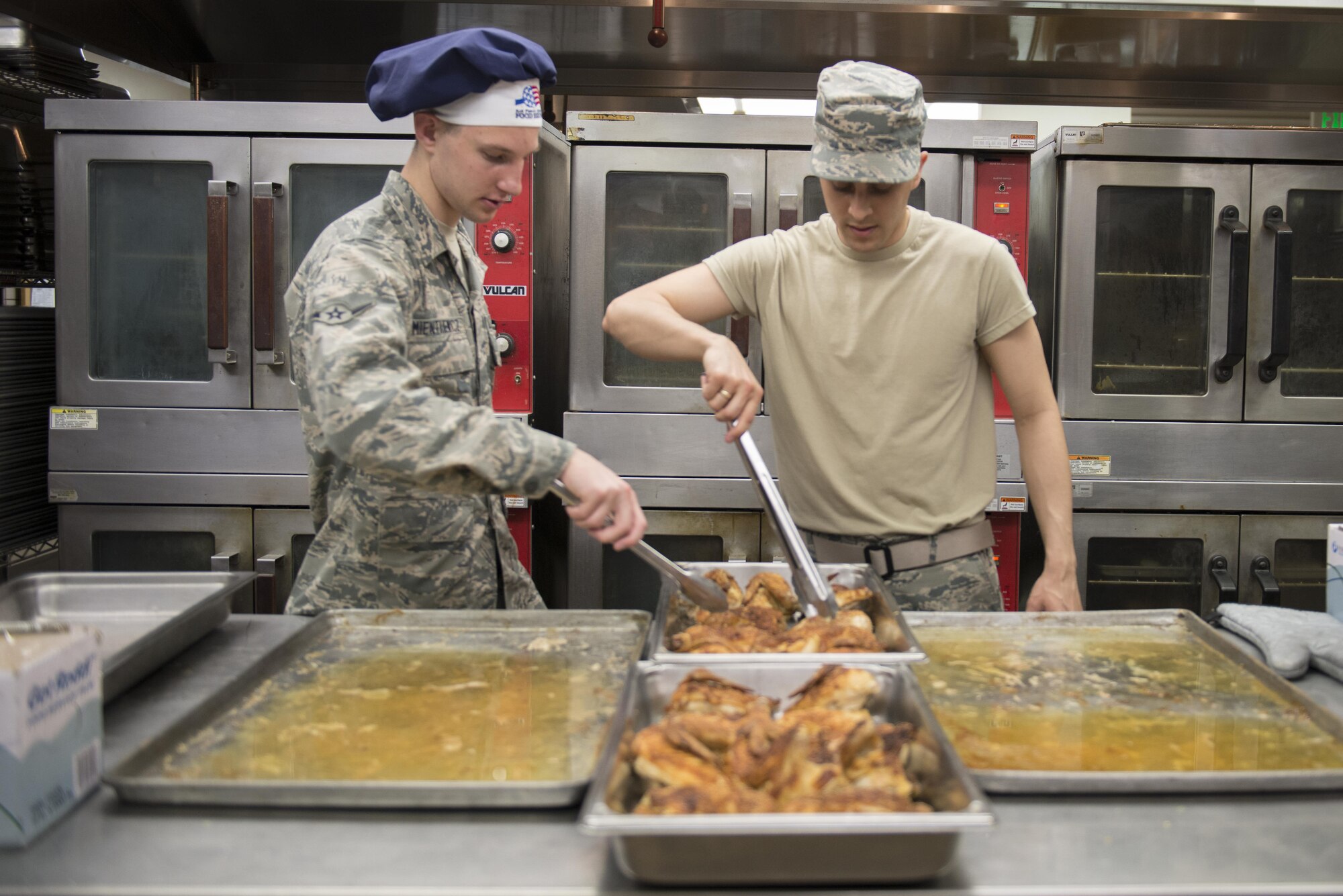 U.S. Air Force Airmen Corry Mientkiewicz and Tyler Morgan, 354th Force Support Squadron services apprentices, prepare 48 pieces of baked chicken for the lunch rush May 11, 2016, at the Two Seasons Dining Facility, Eielson Air Force Base, Alaska. Food services members cooked about twice the amount of food during RED FLAG-Alaska 16-1 than a normal operating day. (U.S. Air Force photo by Staff Sgt. Ashley Nicole Taylor/Released)
