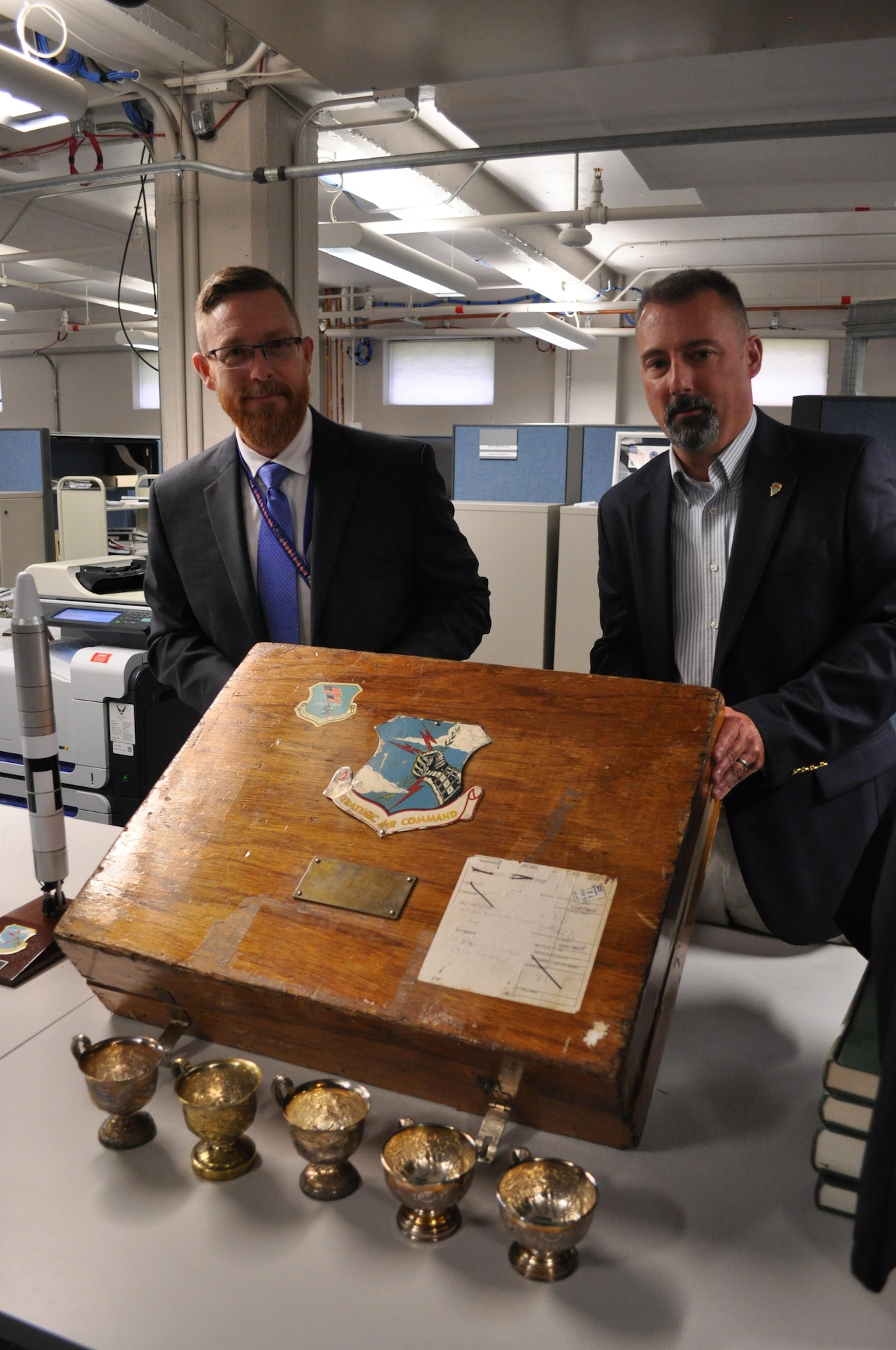 Yancy Mailes, Command Historian, and Shawn Bohannon, Command Archivist, show off a chest containing “bomb com” cups awarded to various Strategic Air Command wings for their annual competition. Several of the cups are displayed in front of the chest. The new Global Strike Research Facility will house these artifacts as well as command archives for both SAC and AFGSC. Staff will have the ability to check out several of these lineage items for command events (Air Force Photo by Joe K. Thomas, Air Force Global Strike Command Public Affairs).