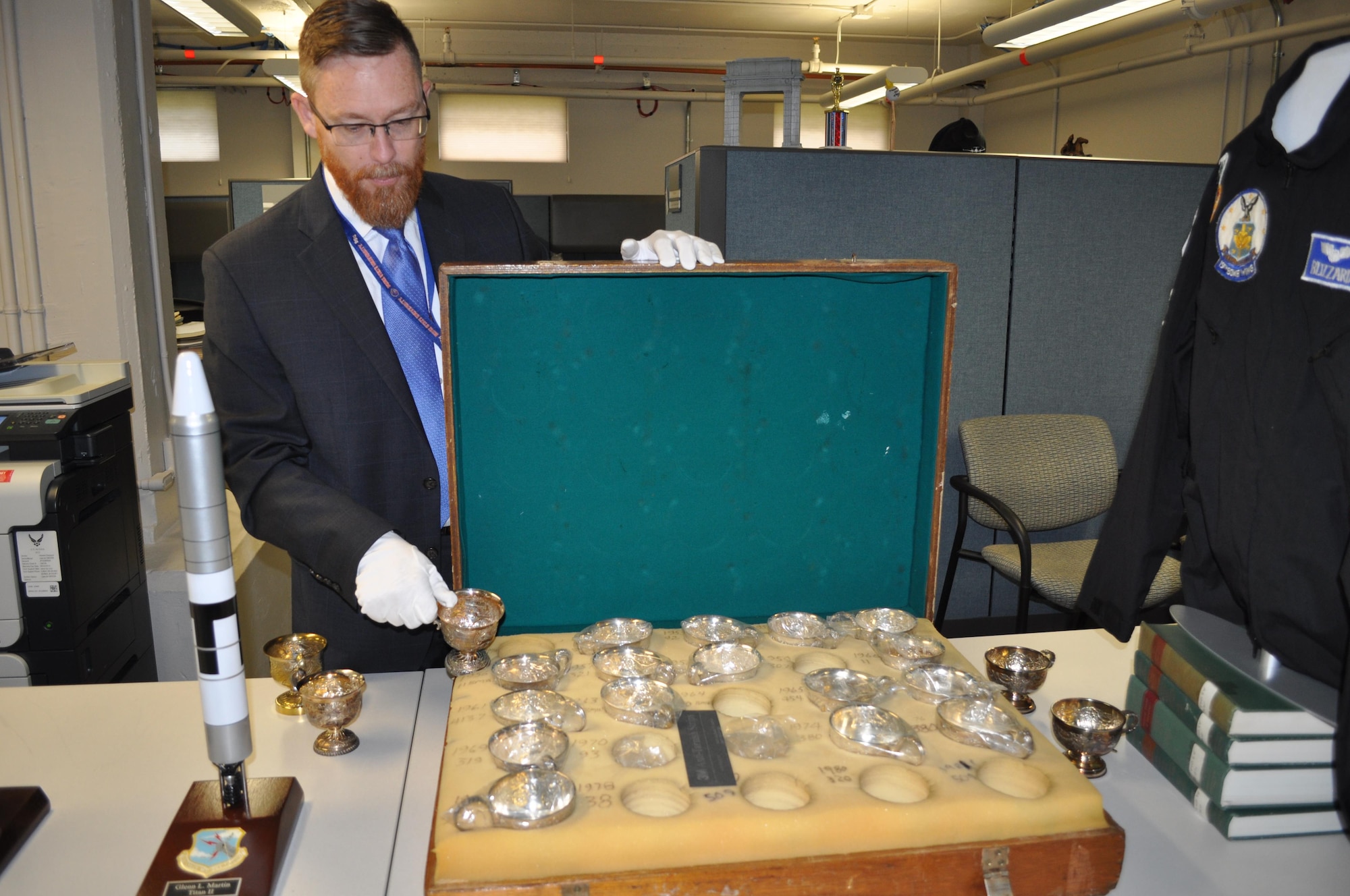 Yancy Mailes, Command Historian, shows off a chest containing “bomb com” cups awarded to various Strategic Air Command wings for their annual competition. Several of the cups are displayed in front of the chest. The new Global Strike Research Facility will house these artifacts as well as command archives for both SAC and AFGSC. Staff will have the ability to check out several of these lineage items for command events (Air Force Photo by TSgt. Ave Young, Air Force Global Strike Command Public Affairs).