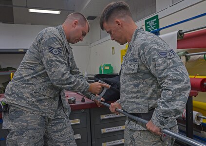 YOKOTA AIR BASE, Japan (May 17, 2016) - Senior Airman Scott Armstrong, 374th Civil Engineer Squadron electrical systems technician, hold part of a raceway pipe as Staff Sgt. Corey Trowbridge, 932nd Civil Engineer Squadron electrical systems technician, from Scott Air Force Base, Illinois, saws it into two pieces at Yokota Air Base.  The electrical flight crew members worked more than 50 man-hours that will save the Aircrew Flight Equipment shop countless hours of life raft inspections helping them turn around the efficiency of being able to produce lifesaving equipment. 