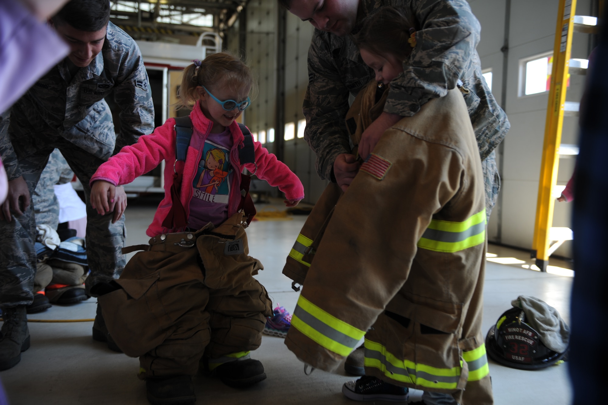 Senior Airman Christopher Smith and Airman 1st Class Brandon Burns, both 5th Civil Engineer Squadron, help children from the Minot Air Force Base Pre School Co-op try on firefighter gear at the Minot AFB fire department on Minot AFB, N.D. May 16, 2016. The Co-op is a group of parents that meet together weekly to teach their kids various school subjects and visited the fire department which was part of several last day events before taking a summer hiatus. (U.S. Air Force photo by Staff Sgt. Chad Trujillo)