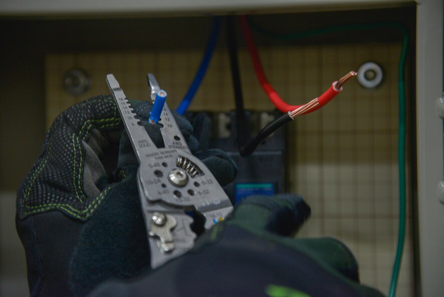 Airman Austin Cartwright, 374th Civil Engineer Squadron electrical systems technician, cuts color-coded insulation off an electrical cable at Yokota Air Base, Japan, May 17, 2016. The motor and new air compressor allows the aircrew flight equipment personnel to inflate and inspect life rafts eight times faster than before. (U.S. Air Force photo by Senior Airman David Owsianka/Released)
