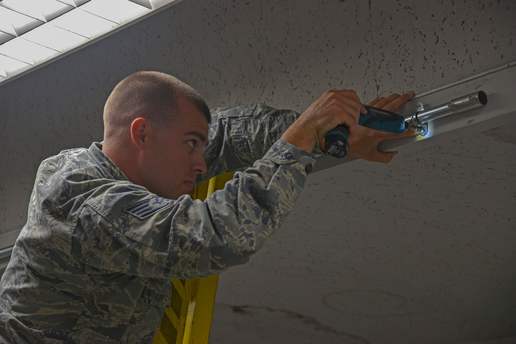 Staff Sgt. Corey Trowbridge, 932nd Civil Engineer Squadron electrical systems technician, from Scott Air Force Base, Illinois, tightens a bolt to hold a raceway pipe in place at Yokota Air Base, Japan, May 17, 2016. The electrical flight crew members worked more than 50 man-hours that will save the Aircrew Flight Equipment shop countless hours of life raft inspections helping them turn around the efficiency of being able to produce life saving equipment. (U.S. Air Force photo by Senior Airman David Owsianka/Released)