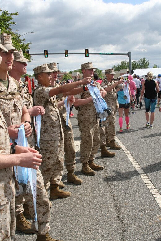Marine Corps lieutenants hold medals at the ready as they cheer on the runners at the finish line.
